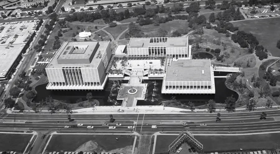 An aerial black-and-white photograph showcases an urban landscape, including buildings, roads, and cars. Infrastructure an...
