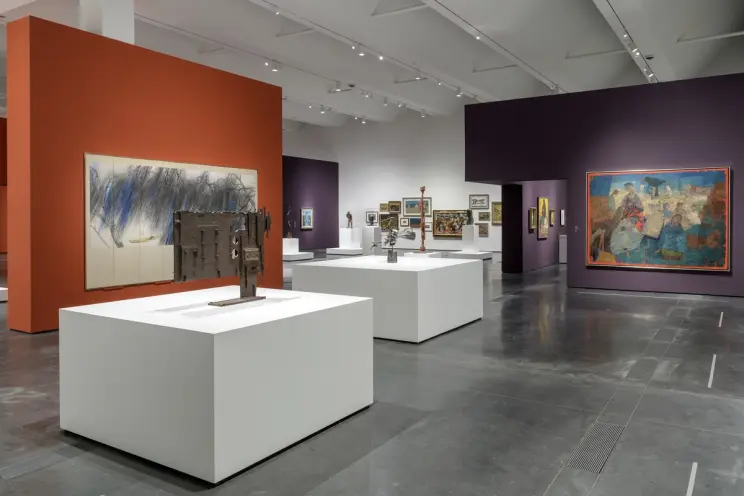 An art gallery room displaying various art pieces on white cubicles positioned centrally. The exhibition walls are splashe...