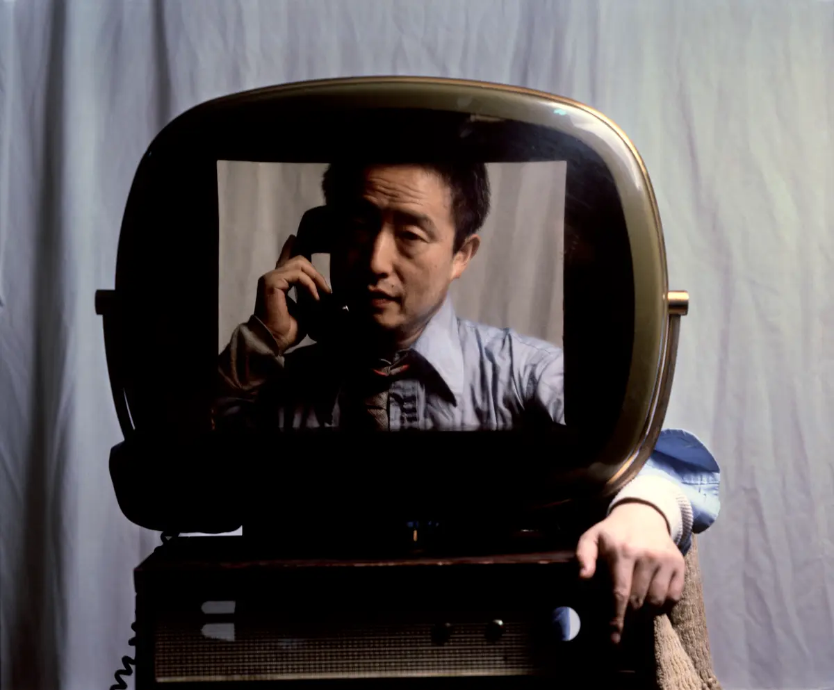 A TV projecting of a man holding a telephone; an arm wraps around from behind the TV.