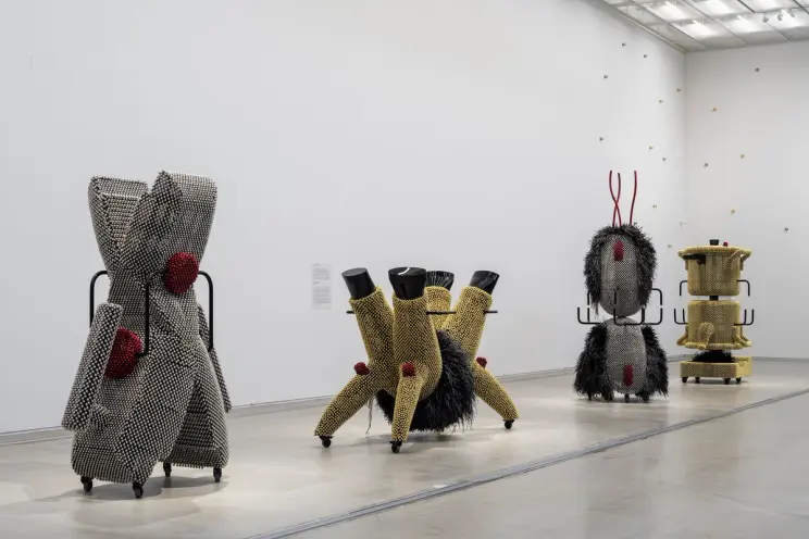 Art installation depicting oversized domestic items, adorned with golden and silver metal pins, conceptually evoking child...