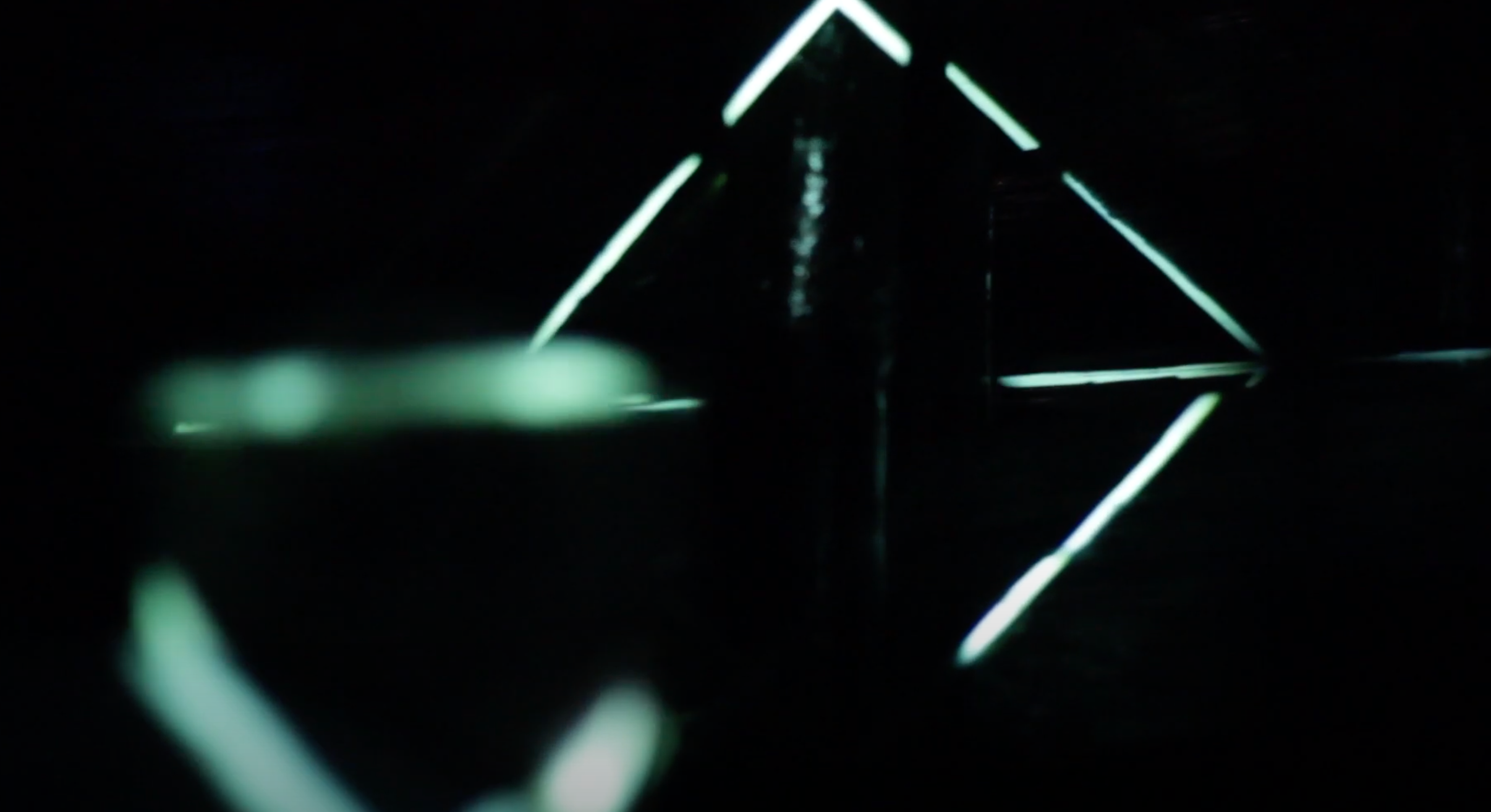 A dark background illuminated by hypnotic green neon light lines in a projection mapping display.