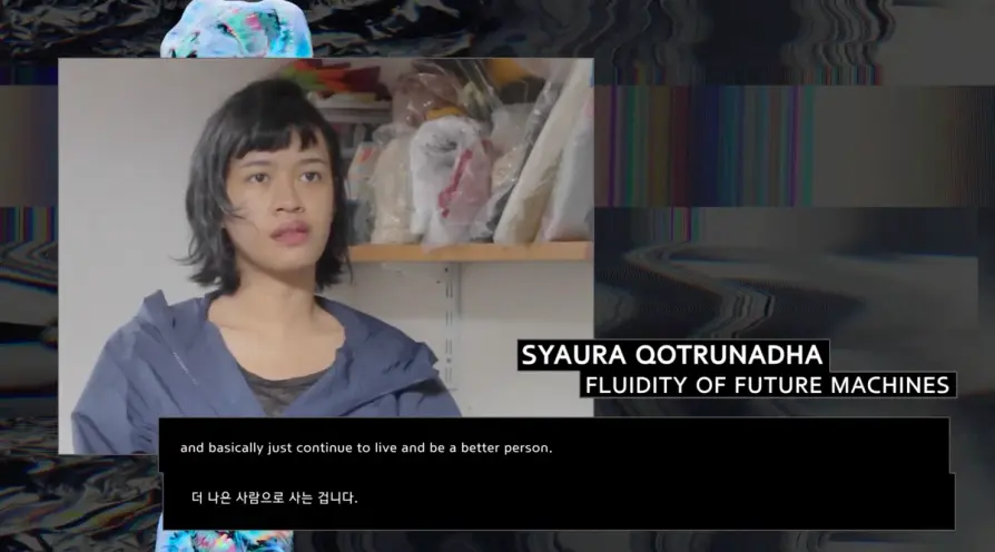 Syaura Qotrunadha speaking to the camera in an interview. They are behind of a caption that reads, "FLUIDITY OF FUTURE MAC...