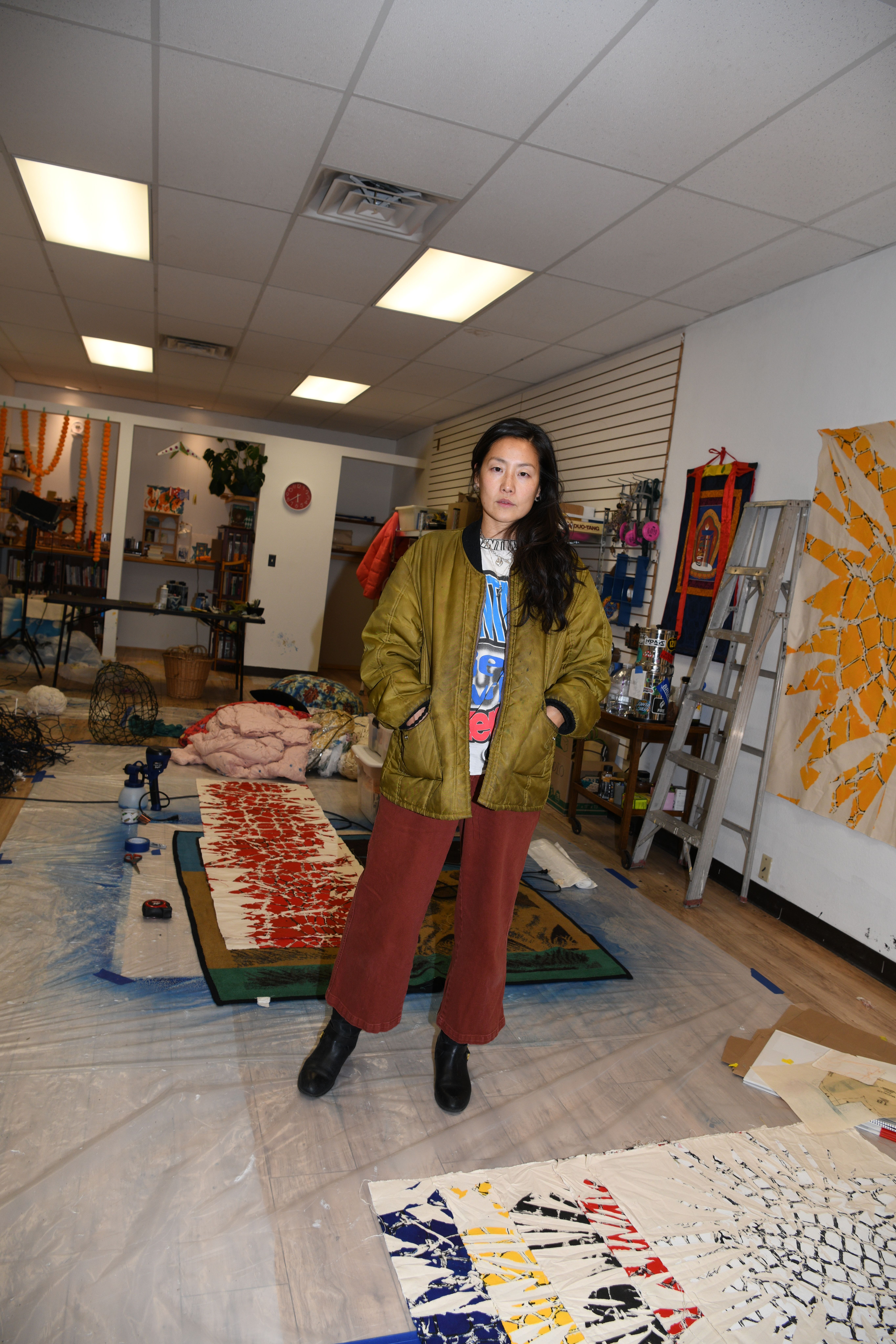 Artist standing in her studio surrounded by colorful artworks and creative materials.