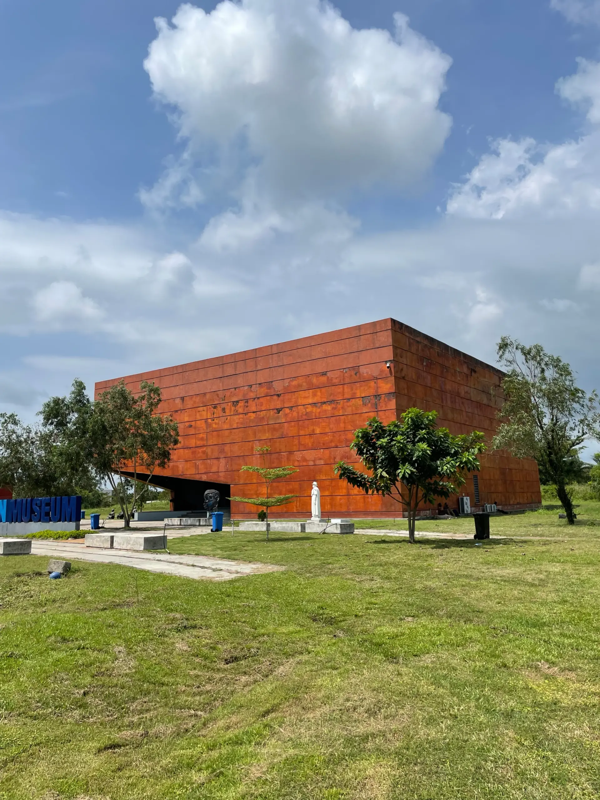 A rust-colored modern museum building surrounded by greenery under a blue sky.