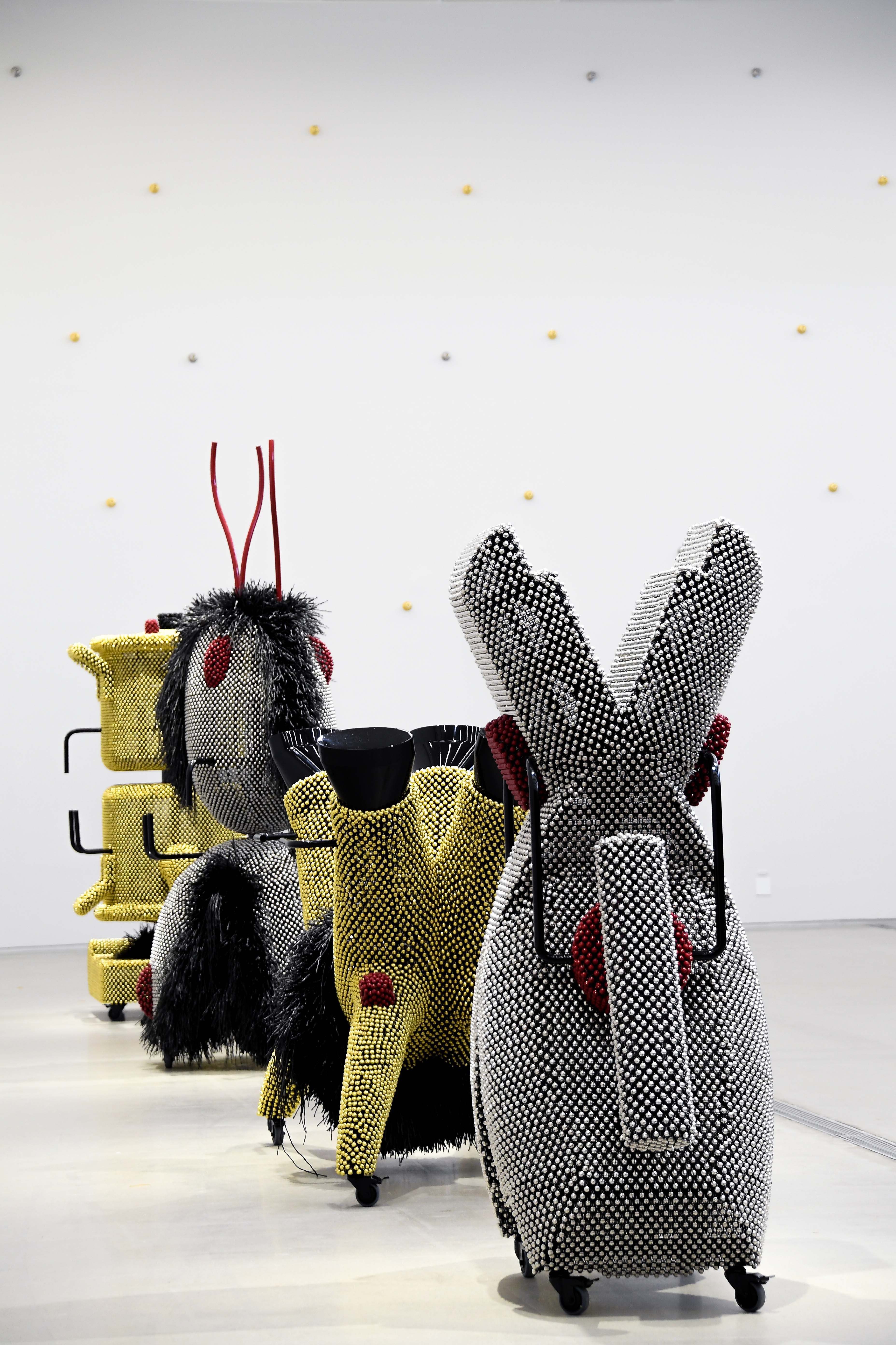 Installation artwork featuring structures adorned with metallic gold and silver pins, reminiscent of toys.