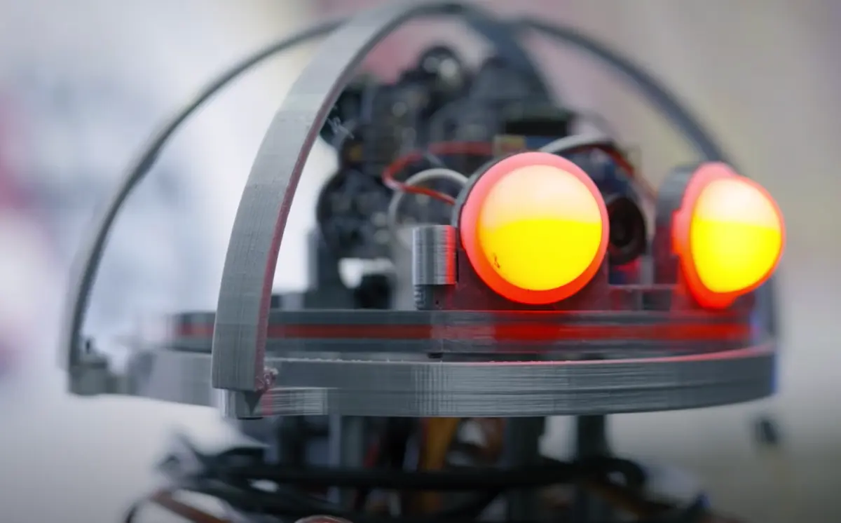 A close-up of a robot's head with glowing red lights functioning as eyes. The focus on the mechanical details of its face gives it a futuristic look.