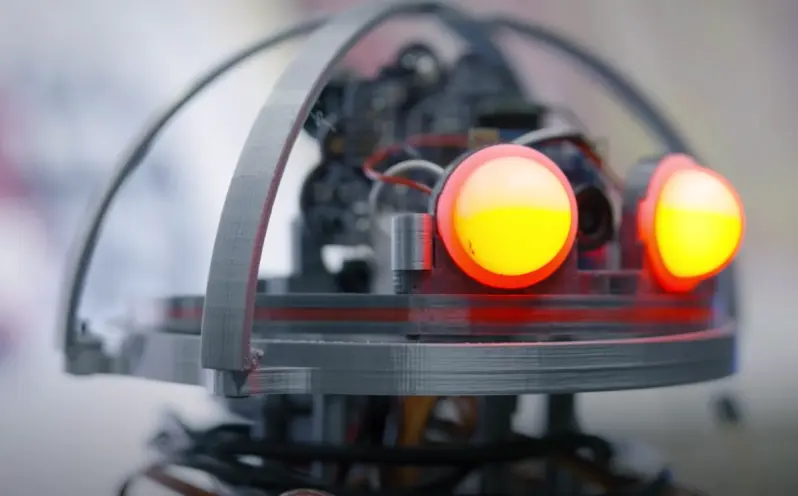 A close-up of a robot's head with glowing red lights functioning as eyes. The focus on the mechanical details of its face ...