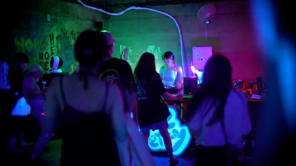 A DJ positioned under neon lights playing music for a dancing crowd.