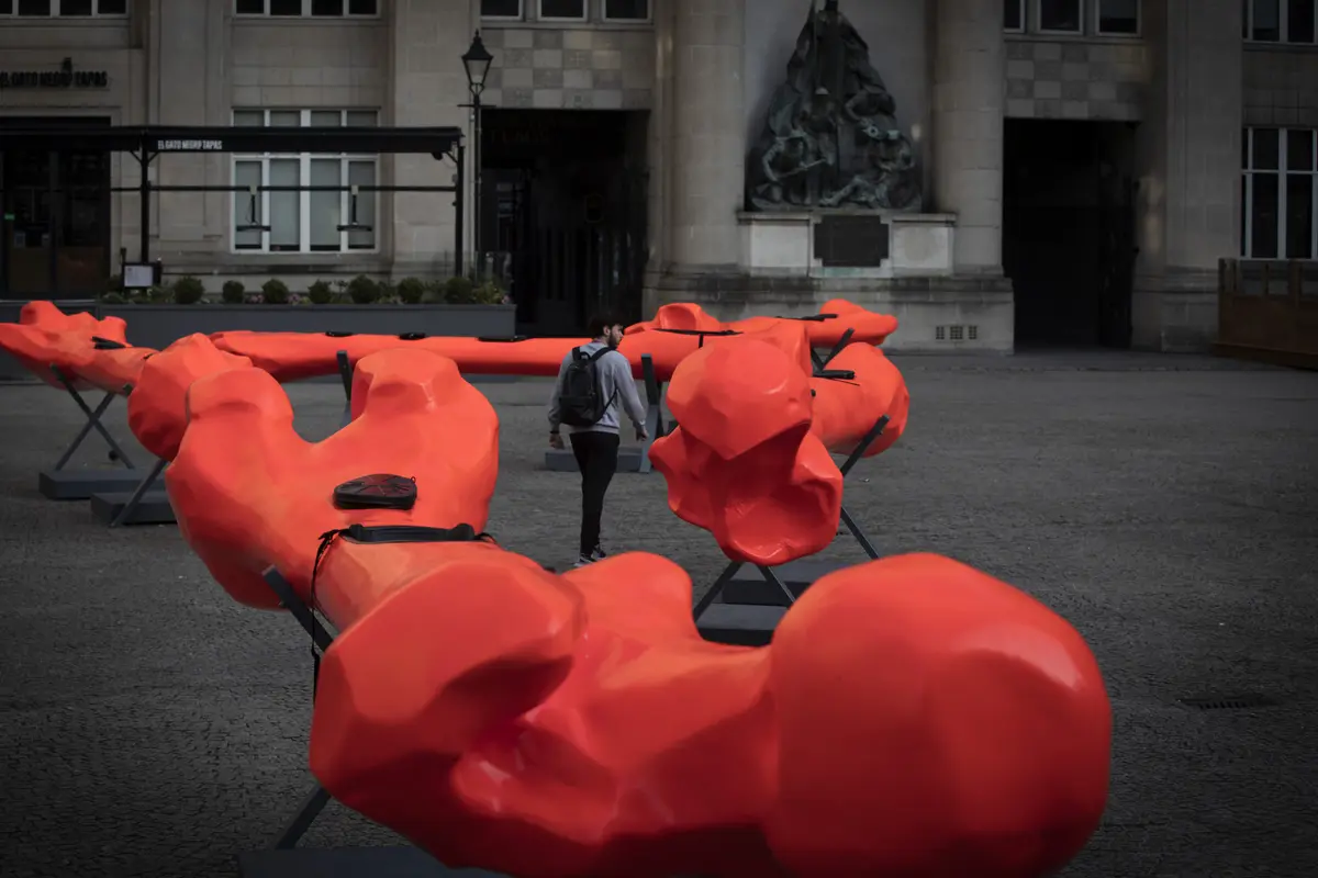 A person walks through a large, red, geometric art installation in an outdoor square.