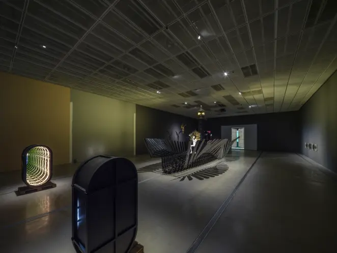 A spacious gallery hall filled with various art installations, including sculptures and paintings, arranged throughout the...