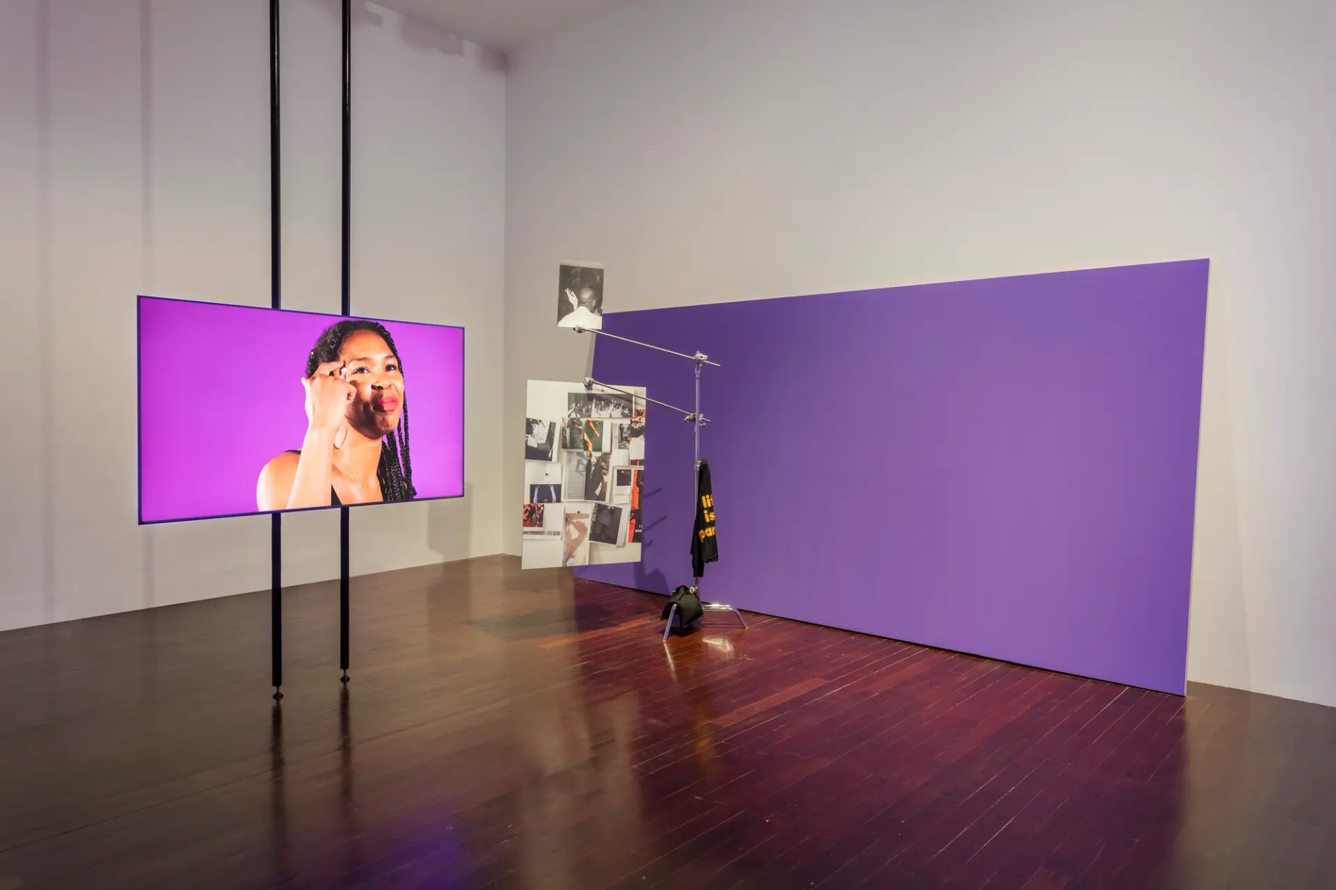 Art installation featuring a large purple rectangle, a photo panel, and a screen displaying an individual against a purple...