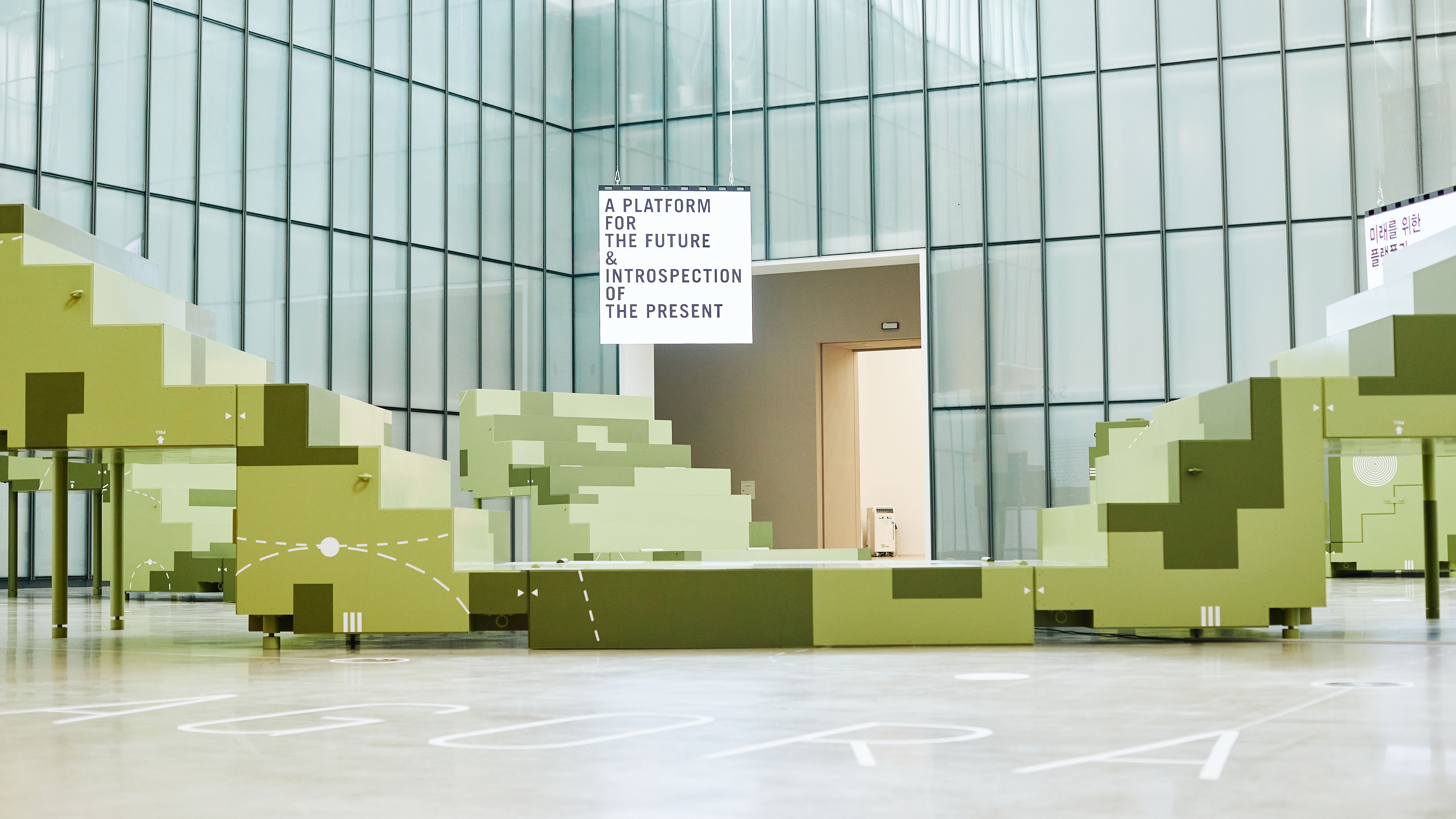 A large stainless steel and aluminum sculpture titled "Mobile Agora" stands in a gallery space. The floor features a paint...