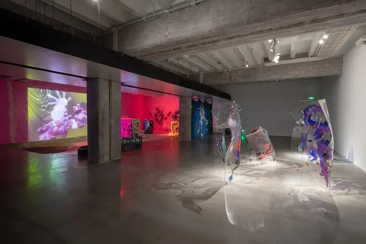 Translucent, water-colored plastic shapes face art projections on the other side of an exhibition room.