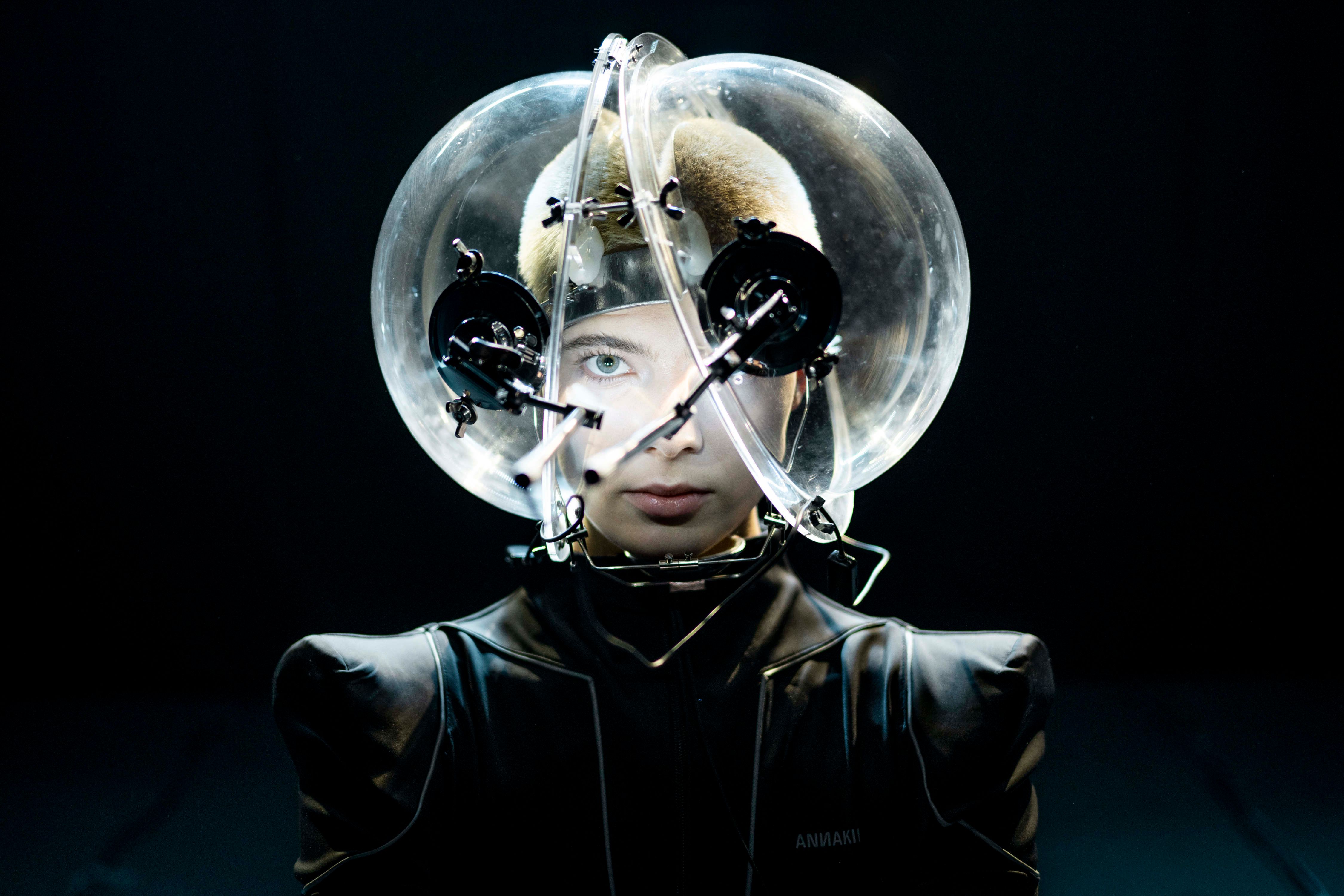 A close-up of a person wearing a futuristic helmet with a transparent sphere enclosing their head, with mechanical attachments.