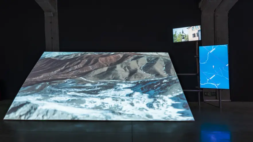 Tilted screen displaying mountain terrain, flanked by two vertical screens.