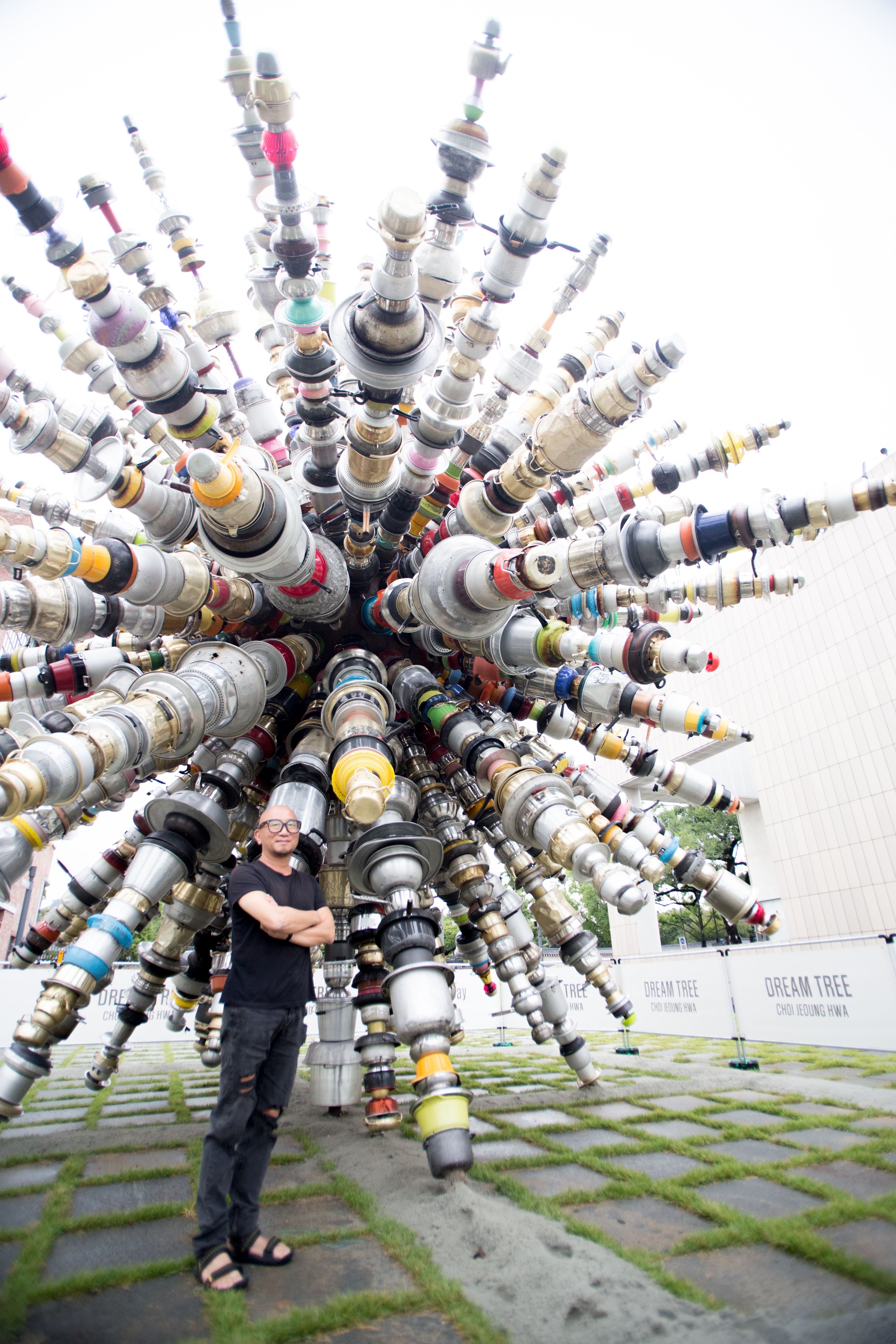 Artist CHOIJEONGHWA standing outside next to a sculpture made of vibrant, protruding segments.