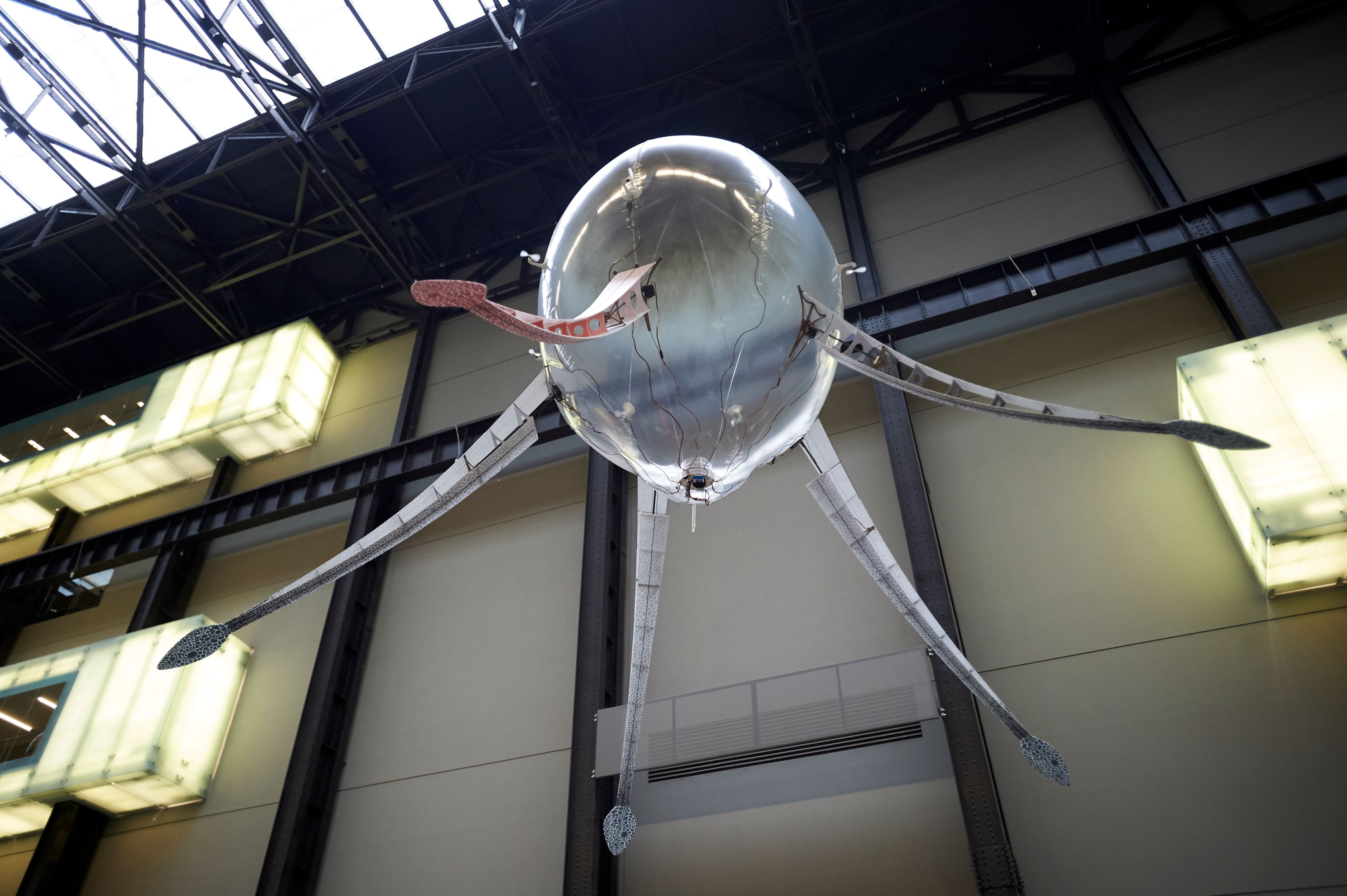 A ceiling lamp designed like an octopus with snake-headed tentacles hangs in a large gallery space.
