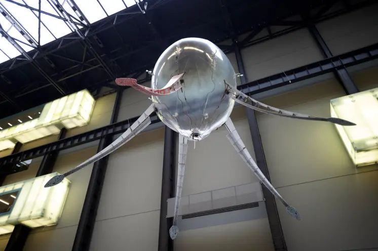 A ceiling lamp designed like an octopus with snake-headed tentacles hangs in a large gallery space.
