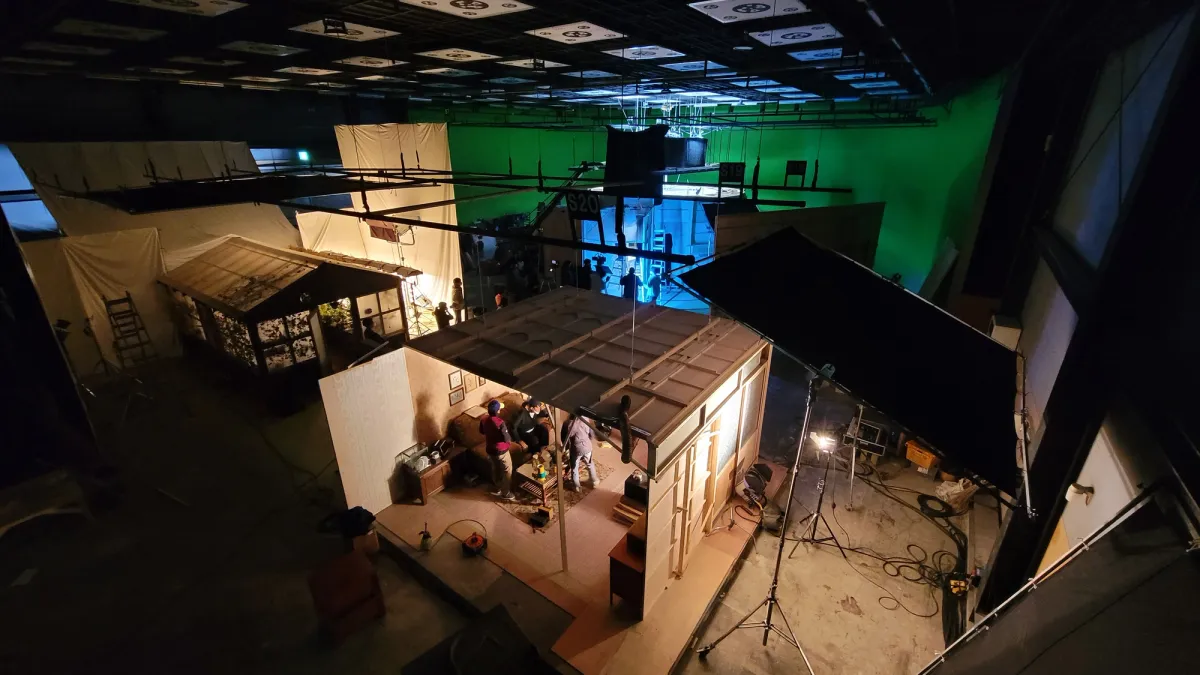 An overhead view of a large television studio with various indoor sets, bathed in a dim, atmospheric lighting.