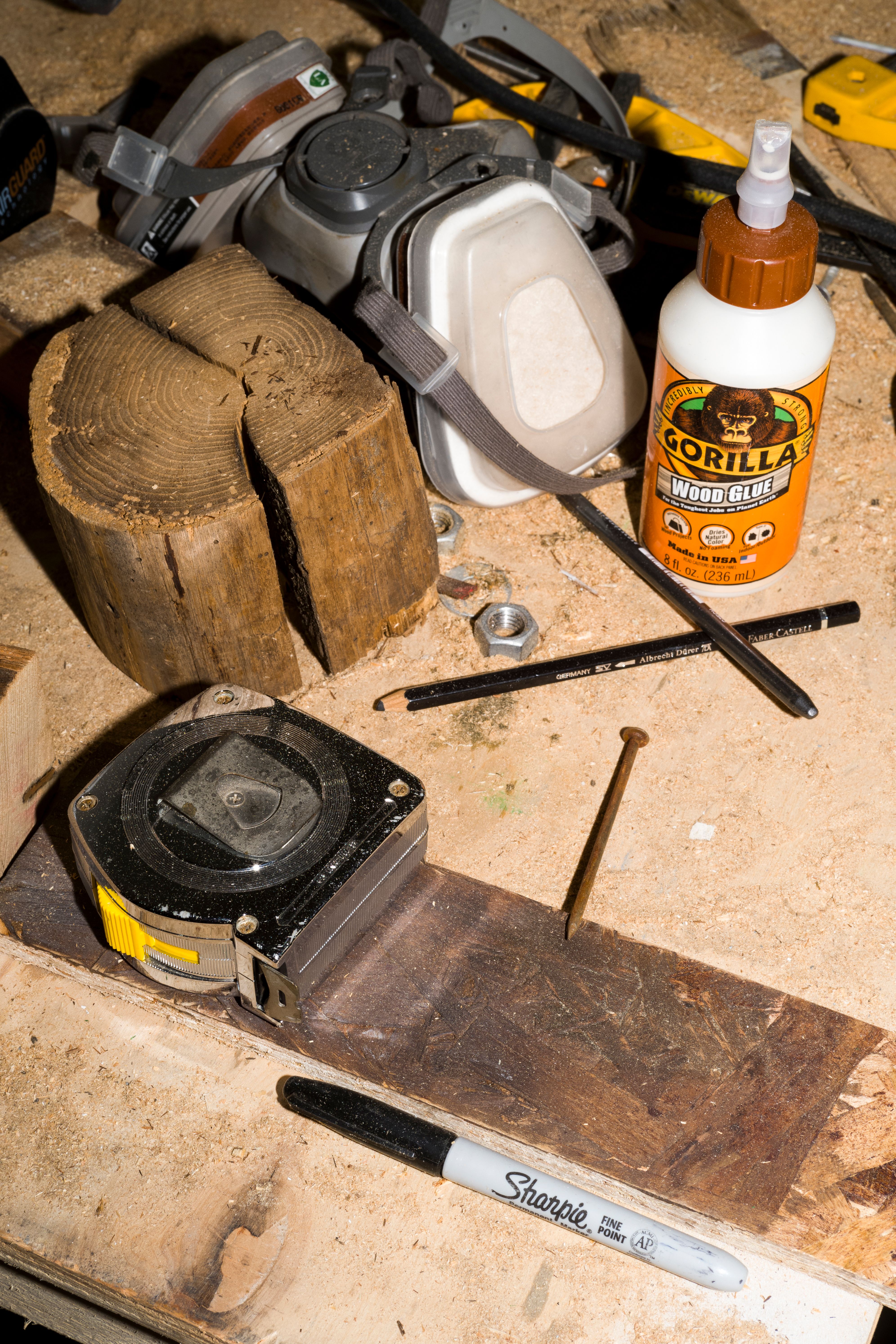 Workbench with tools: tape measure, wood glue, Sharpie, respirator mask, wood, nail, and pencil.