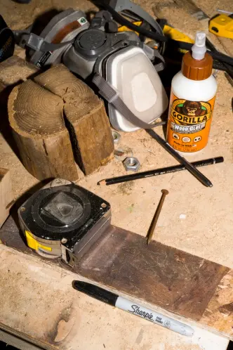 Workbench with tools: tape measure, wood glue, Sharpie, respirator mask, wood, nail, and pencil.
