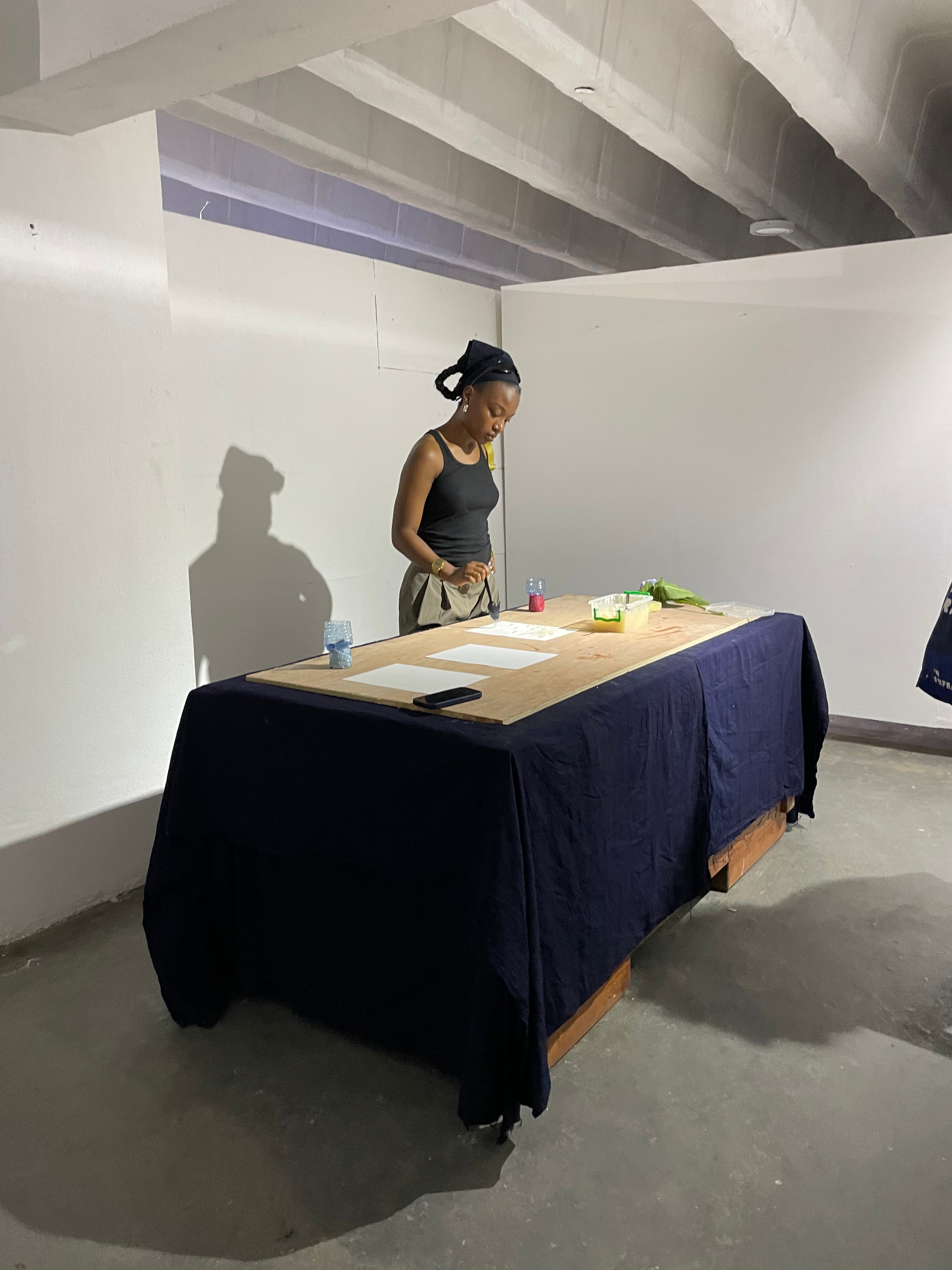 A woman conducting an activity or performance at a table in a minimalist indoor space.