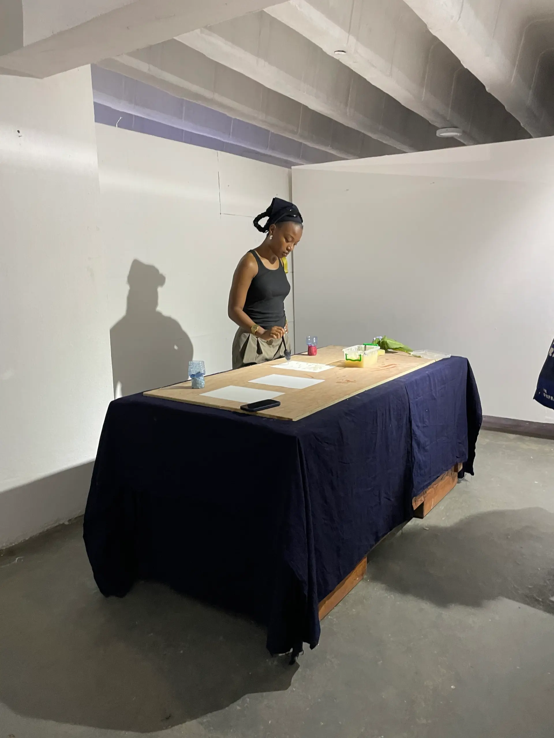 A woman conducting an activity or performance at a table in a minimalist indoor space.
