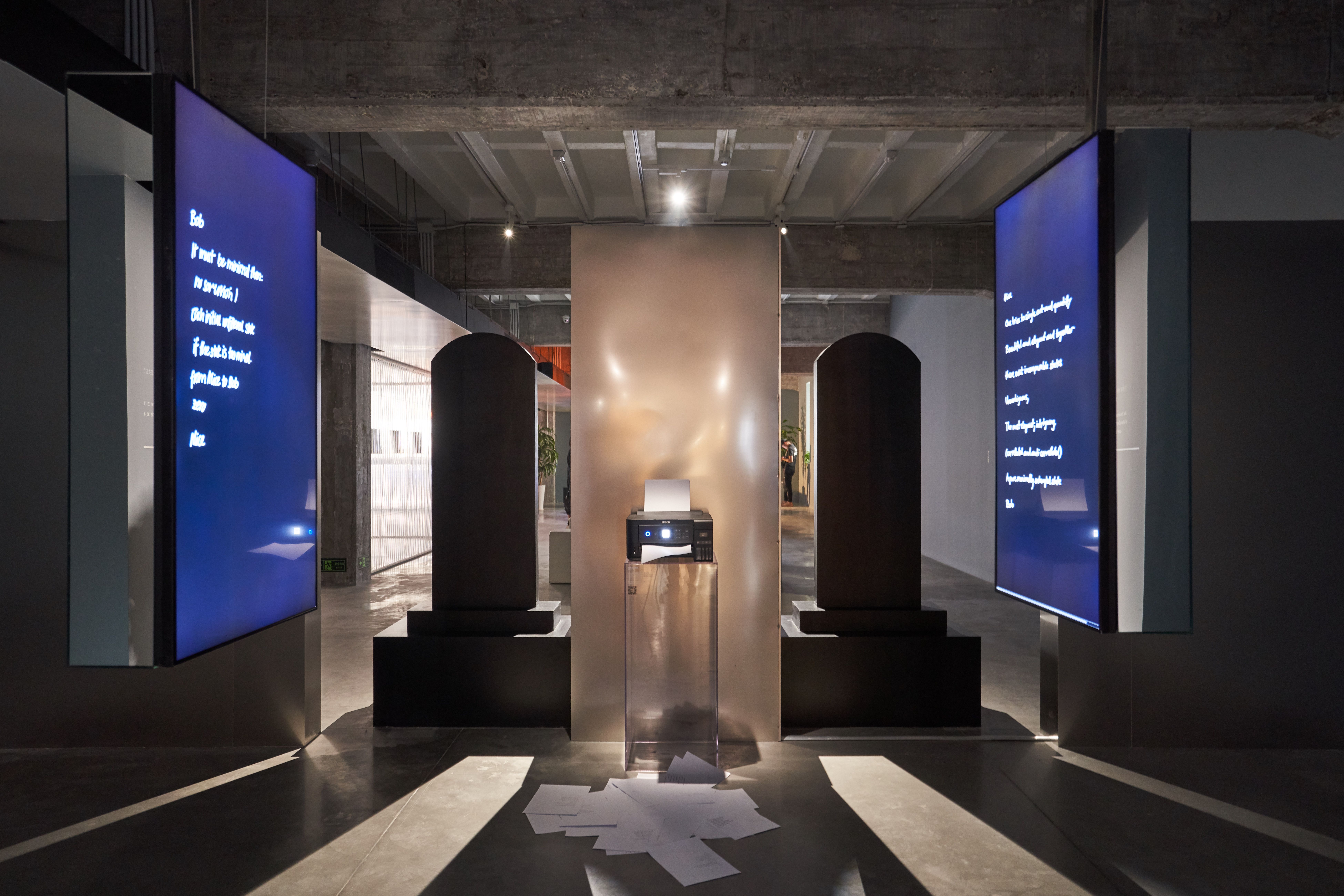 Screens with text and printer on display in art installation.