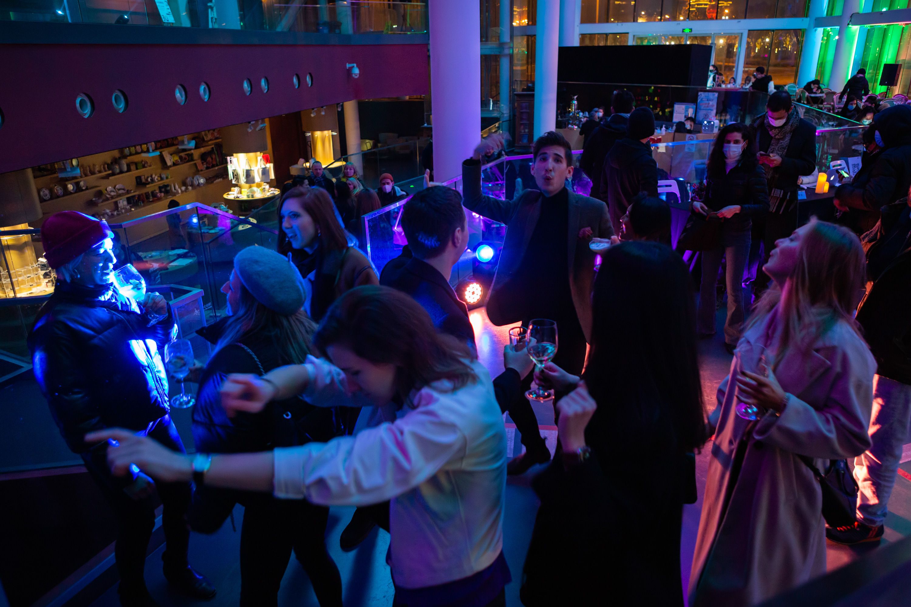 A bustling indoor party at the Yuz Museum, with a crowd of people engaged in dancing, illuminated by warm party lights.
