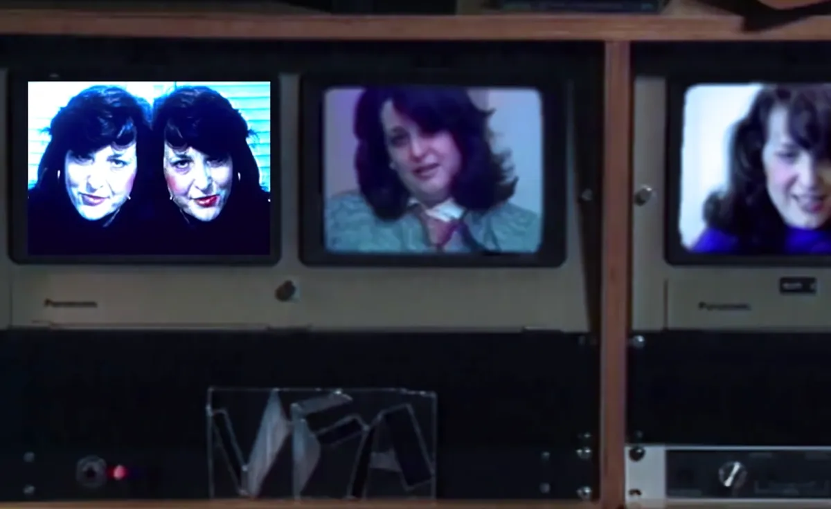 An image from "Electronic Diaries" featuring Lynn Hershman on a dated electronic device with a background full of retro computer equipment.