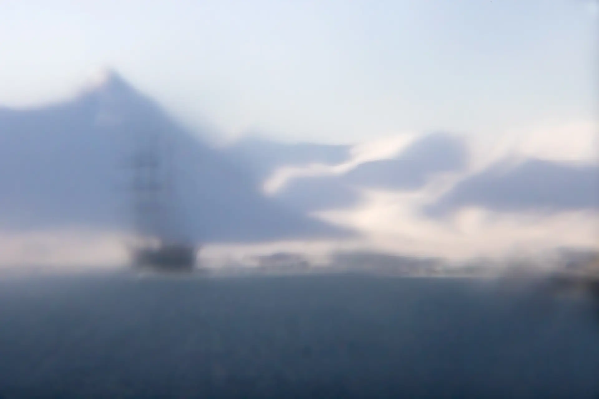A blurred photo of a sea with a ship, encompassed by large snowy mountains.