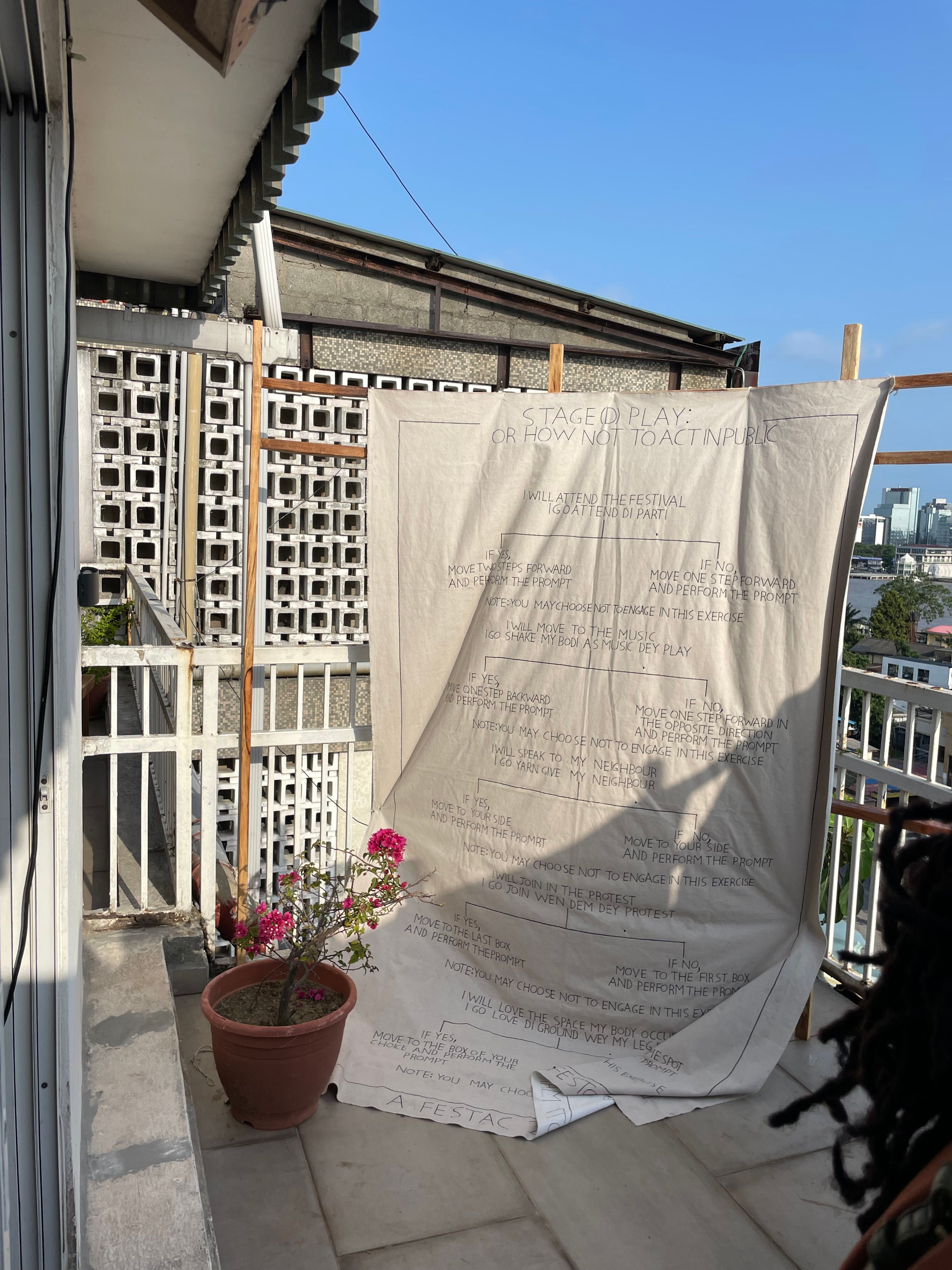 A handwritten text-based art installation on fabric displayed on a sunlit balcony.