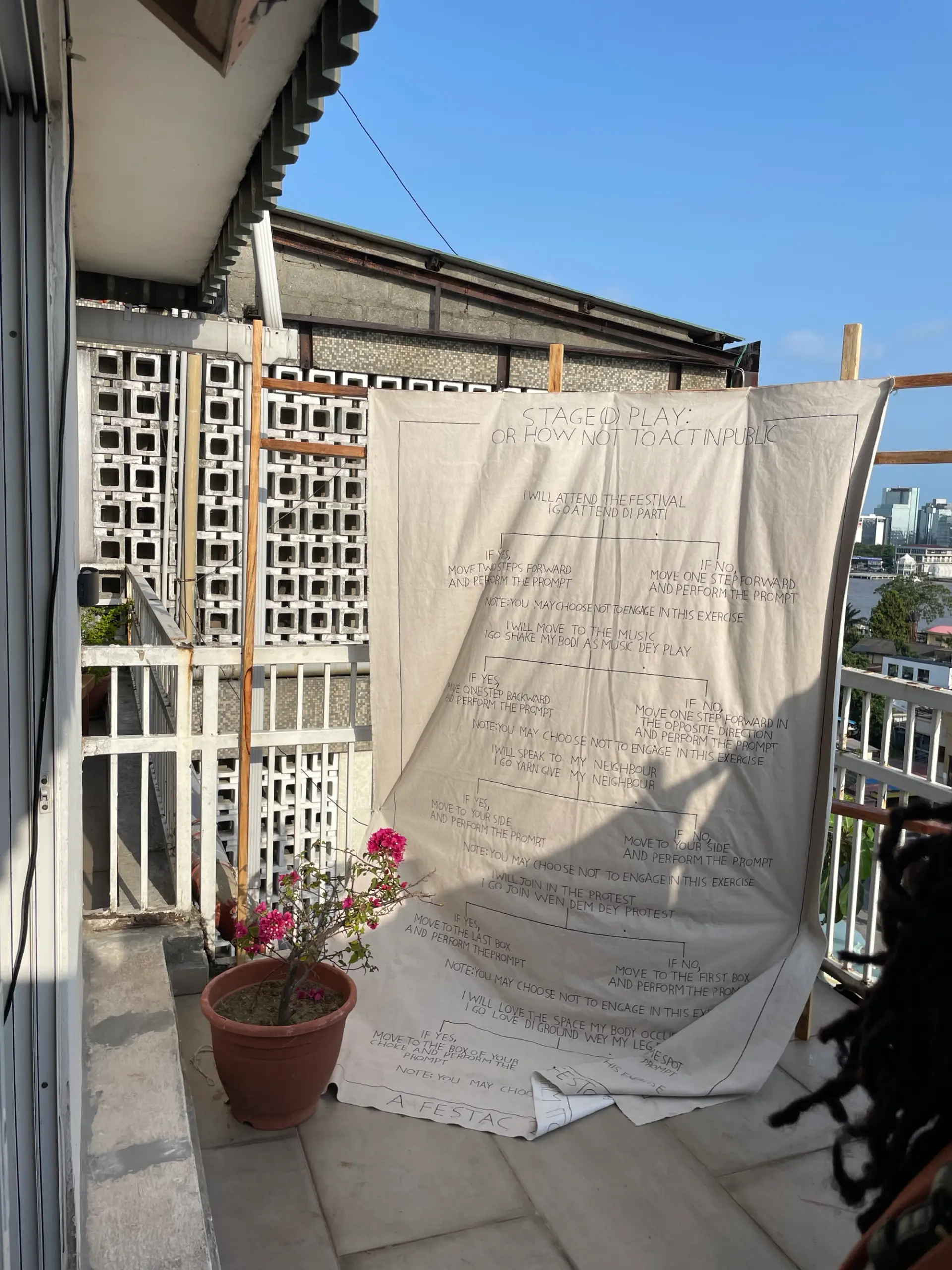 A handwritten text-based art installation on fabric displayed on a sunlit balcony.