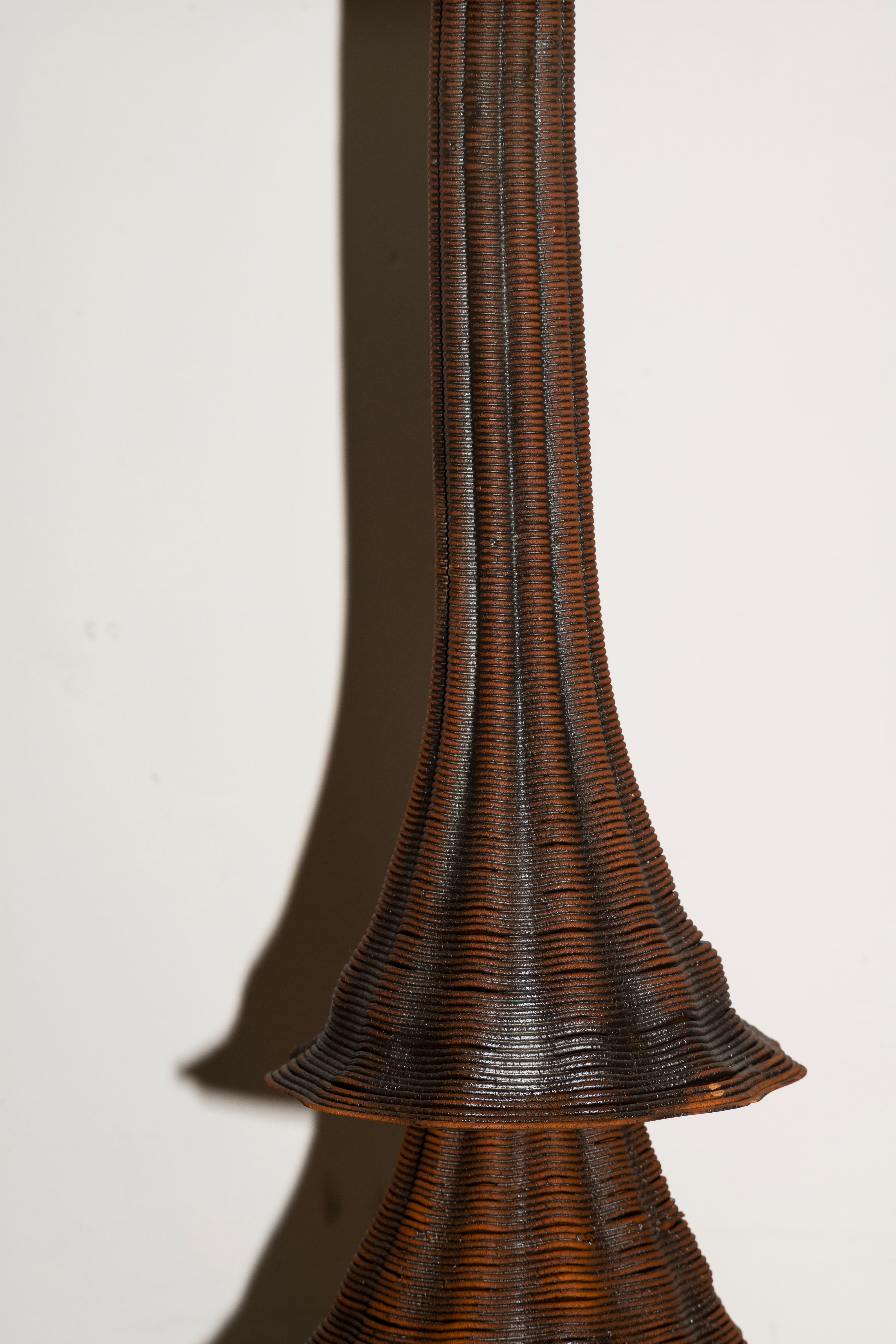 A close-up of a tall, sculpted object with a ribbed, organic texture in warm bronze tones.