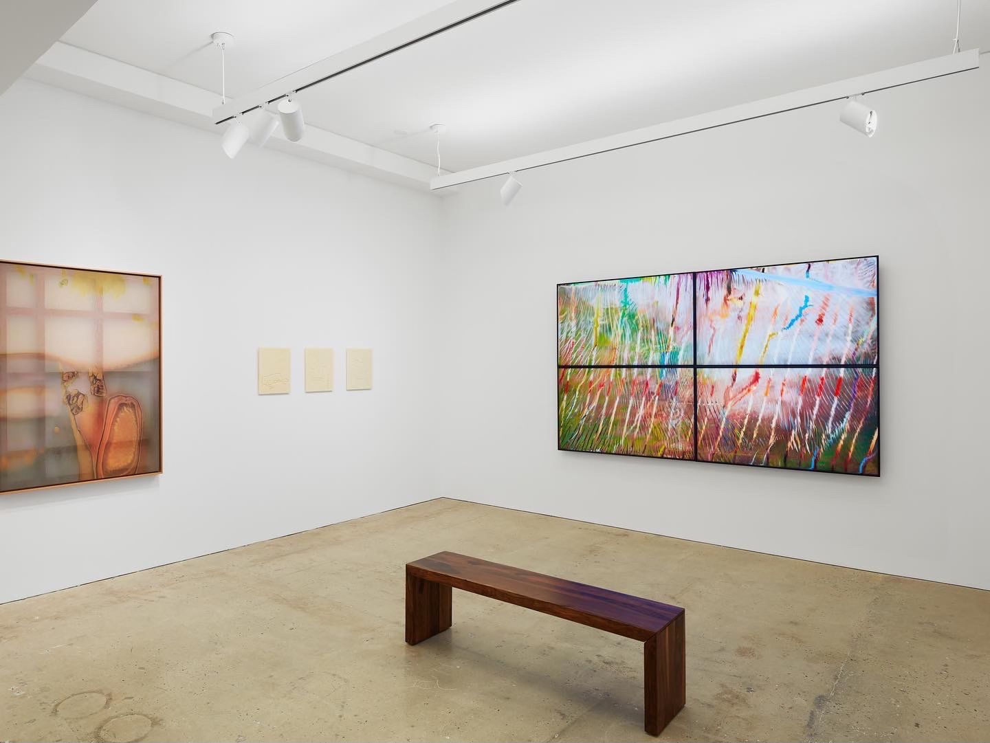 A bench positioned in the center of a brightly lit gallery, surrounded by various paintings on the walls.