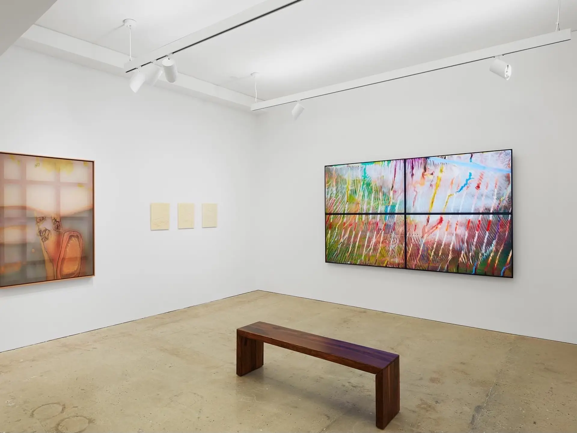 A bench positioned in the center of a brightly lit gallery, surrounded by various paintings on the walls.