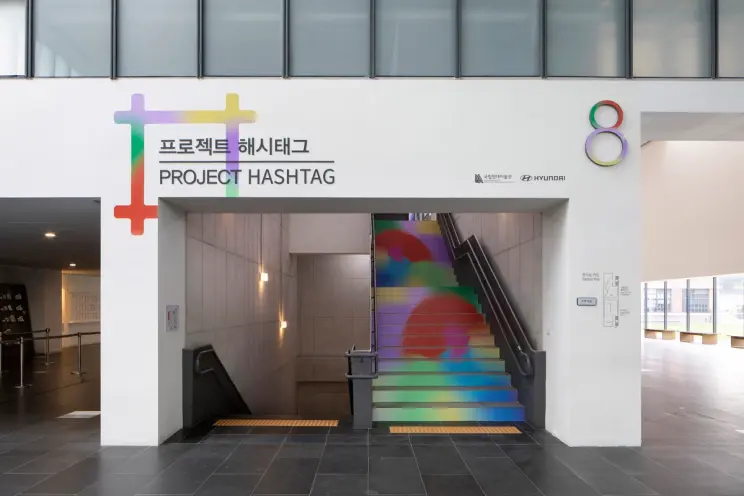 A poster for PROJECT HASHTAG 2020 is prominently displayed in a metro station near the stairs.