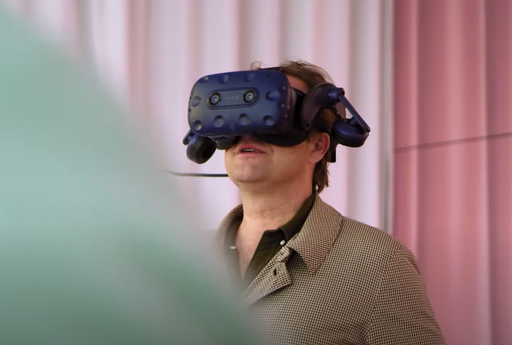 A person donned in a virtual reality headset stands against a backdrop of pink walls, their expression showing amusement.