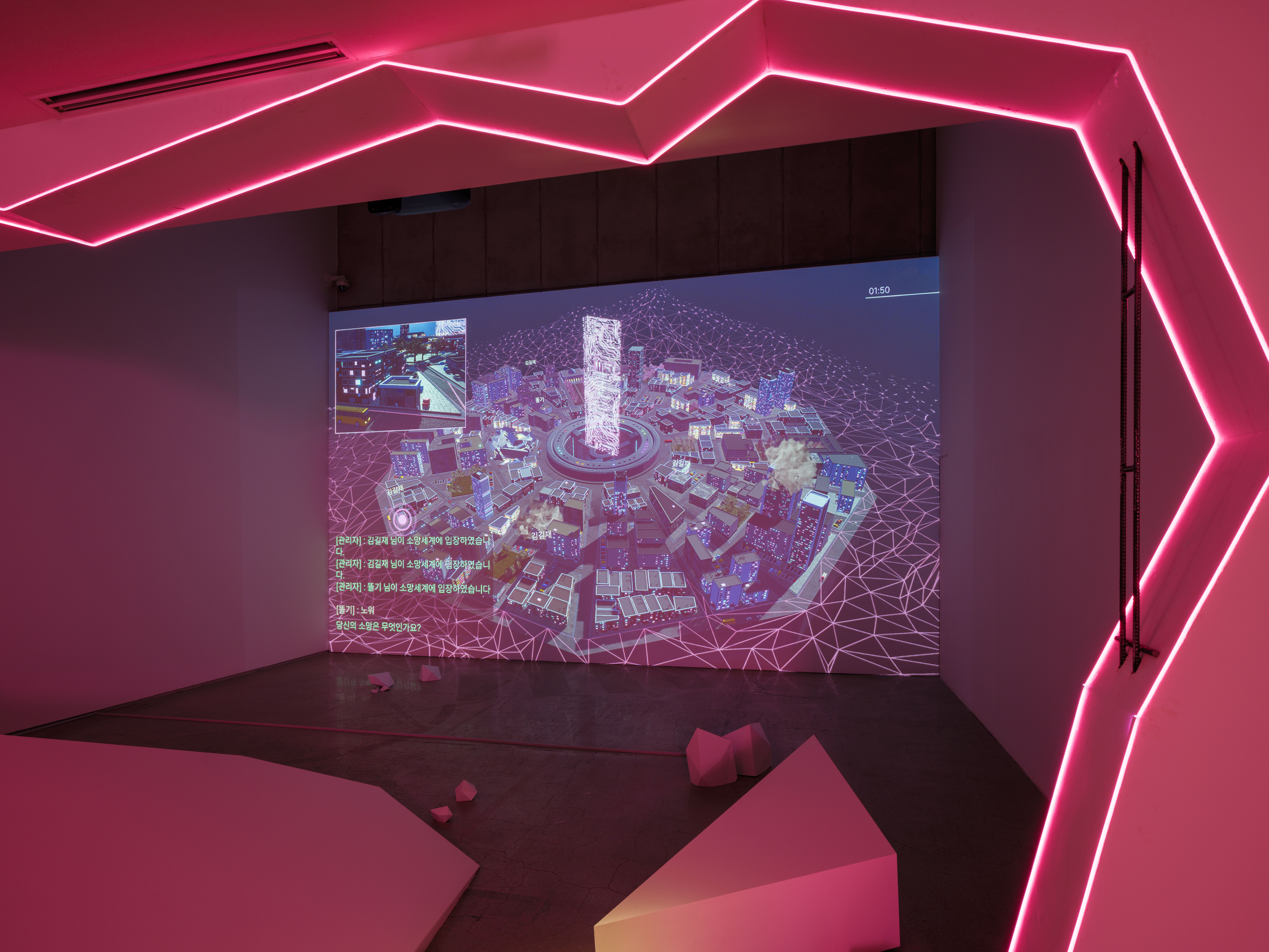 A darkened gallery lit by pink neon outlining a jagged hexagonal frame. A digital projection of a virtual cityscape with K...