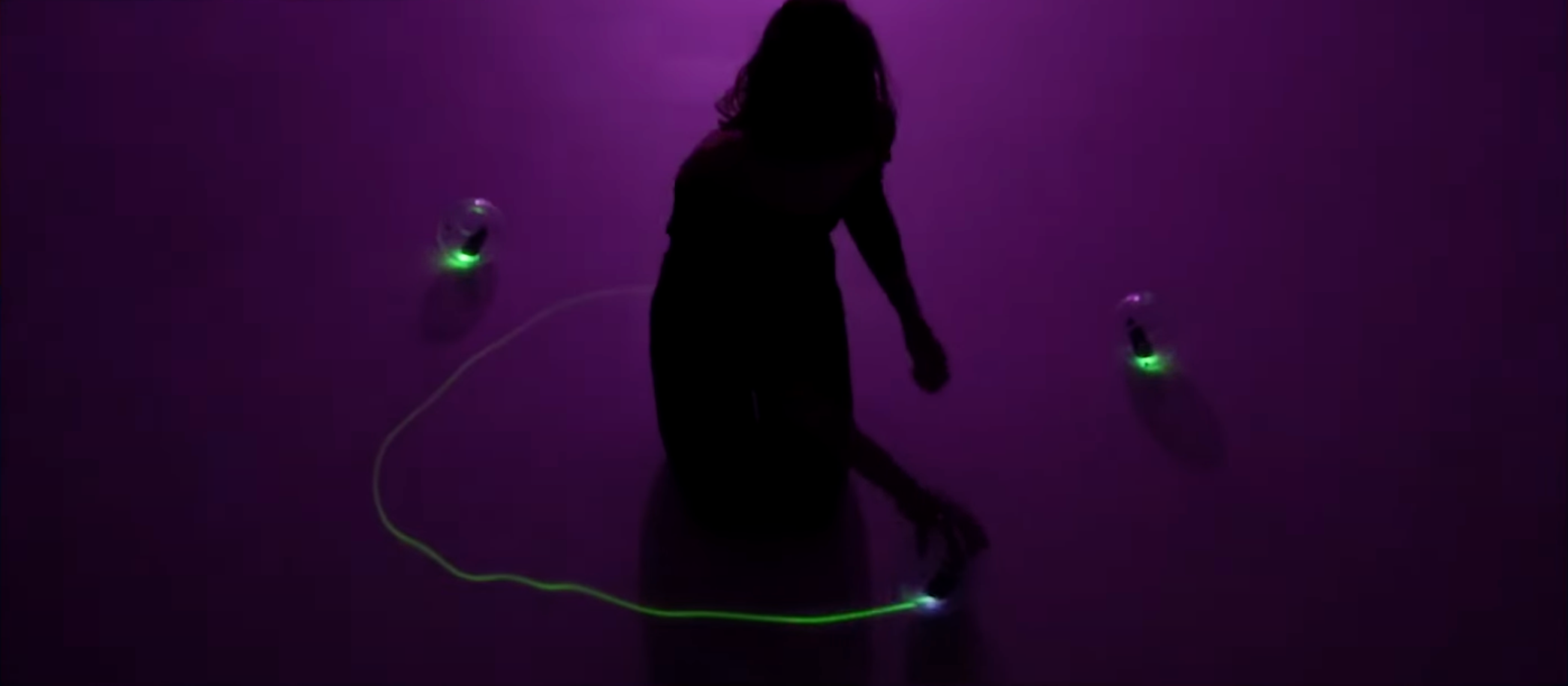 A silhouette of a person against a deep purple background, engaged with objects that emanate a green glow.