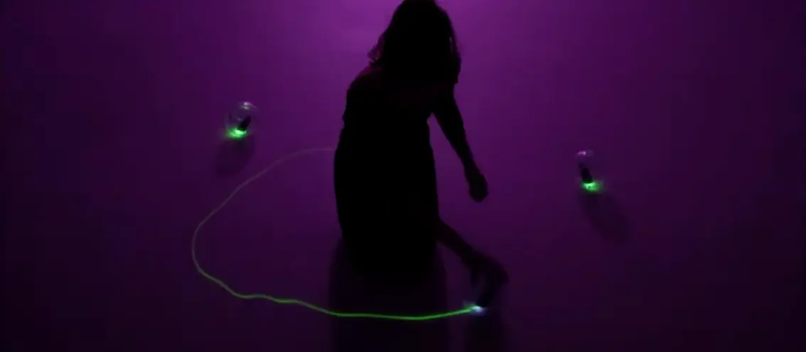 A silhouette of a person against a deep purple background, engaged with objects that emanate a green glow.
