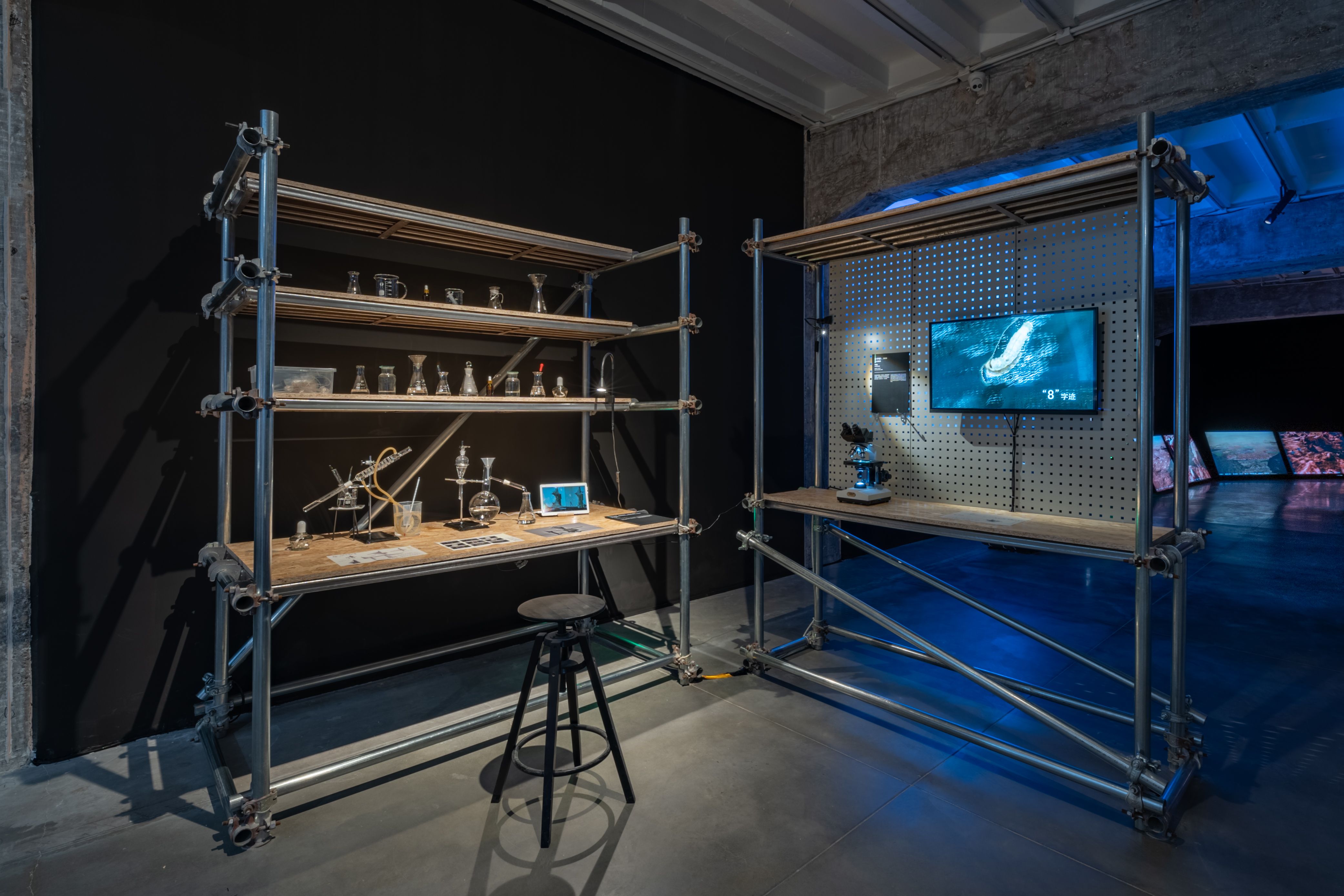 Industrial-style display shelves with various scientific objects and a screen.