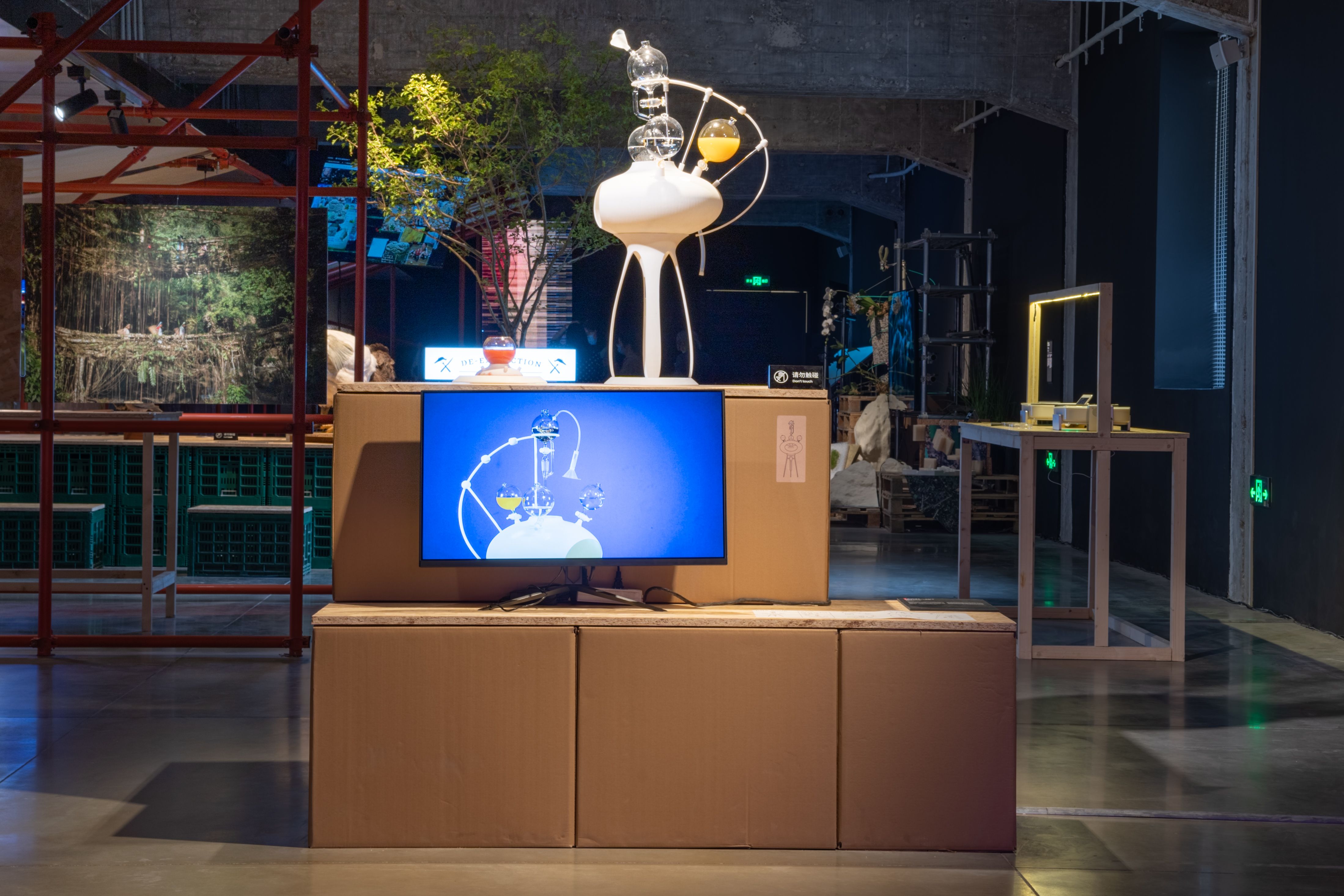 Artistic display with sculptures, a monitor, and cardboard boxes.