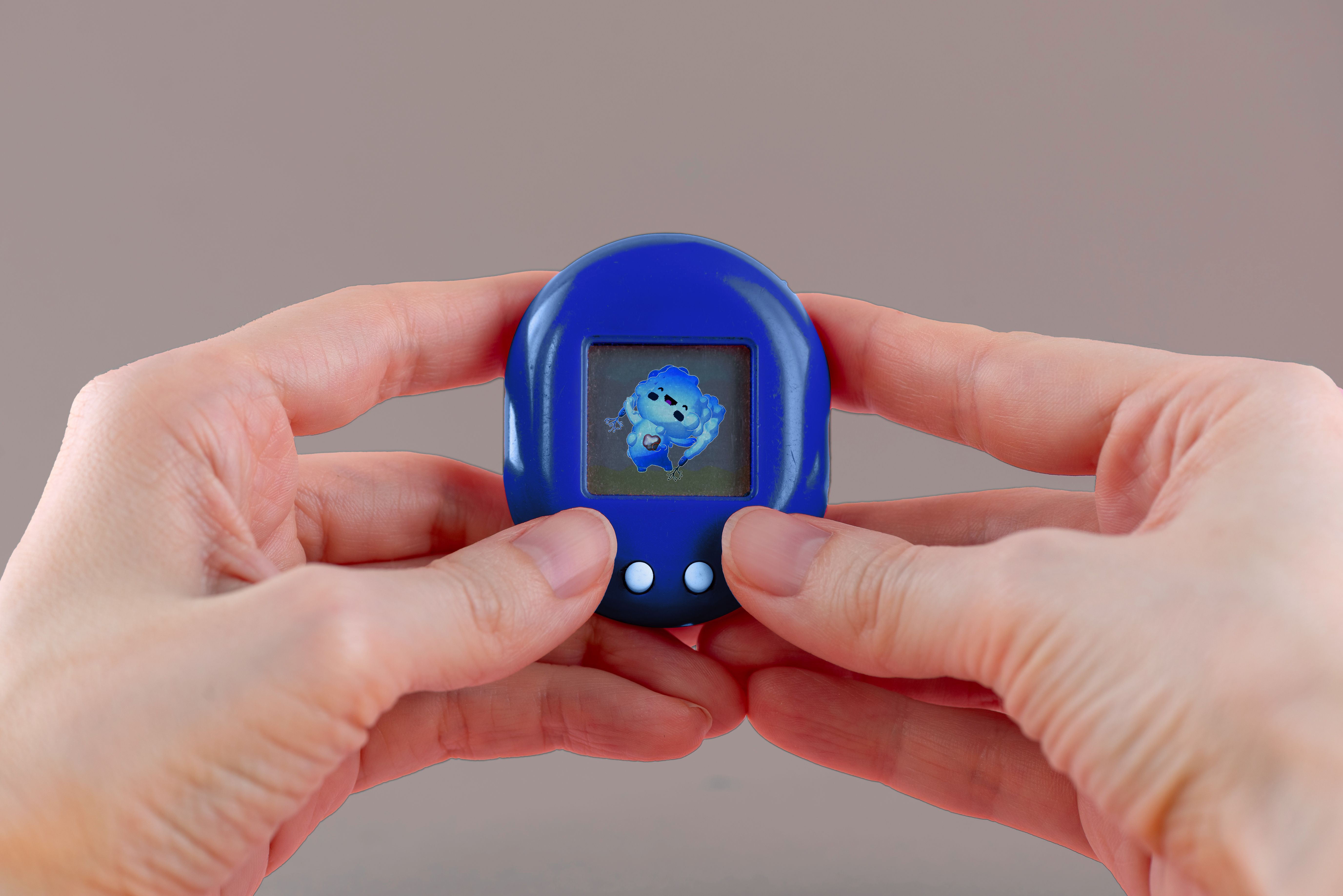 Hands holding a small, blue digital pet device with an animated blue character on the screen.