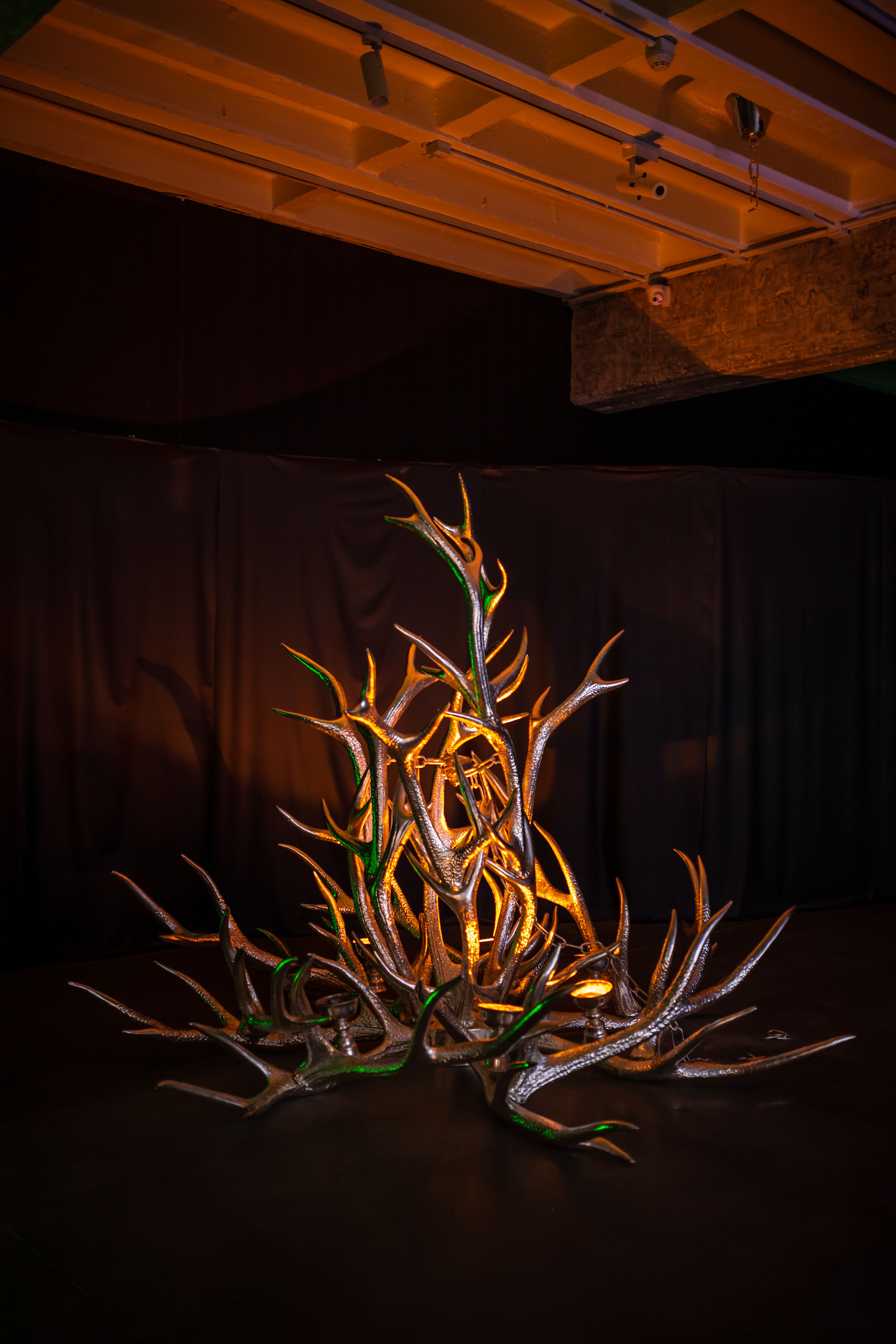 Sculpture of a golden and green metallic plant-like structure on a dark background.