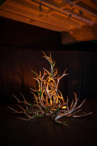Sculpture of a golden and green metallic plant-like structure on a dark background.