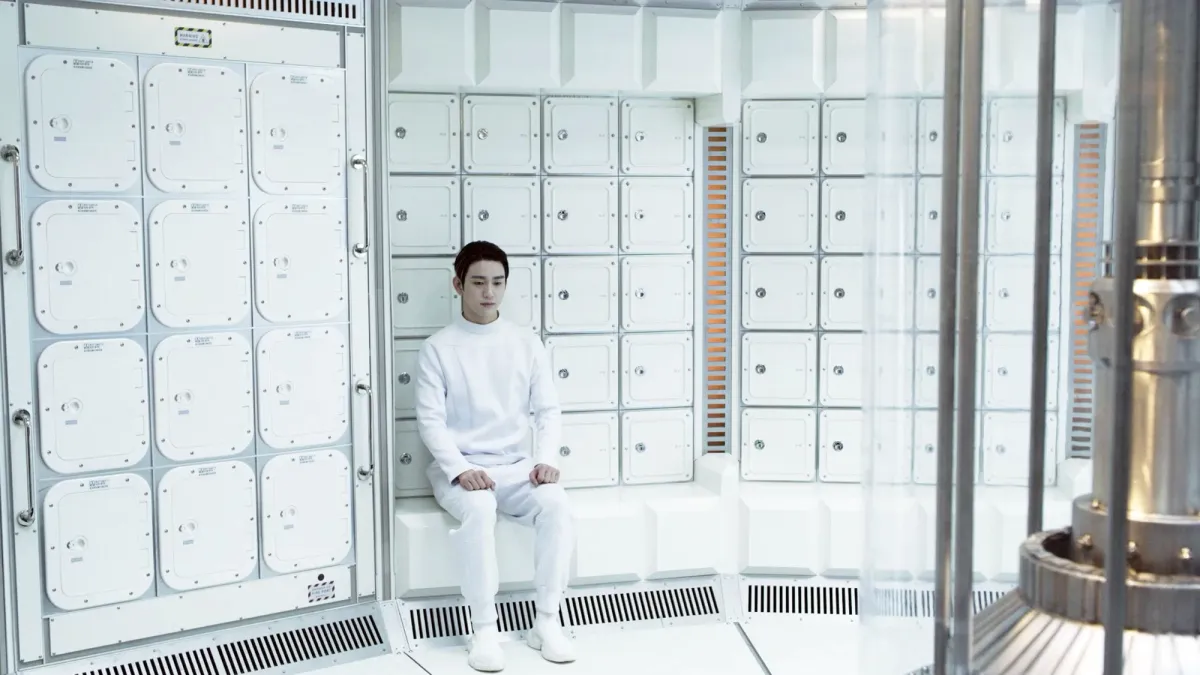An individual dressed in white sitting in a futuristic, sci-fi style room with white interiors and sleek design.