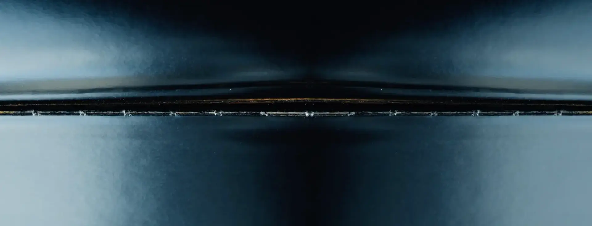 A dark blue and black horizontal form emerges from a surrounding darkness, creating a sense of depth and mystery.