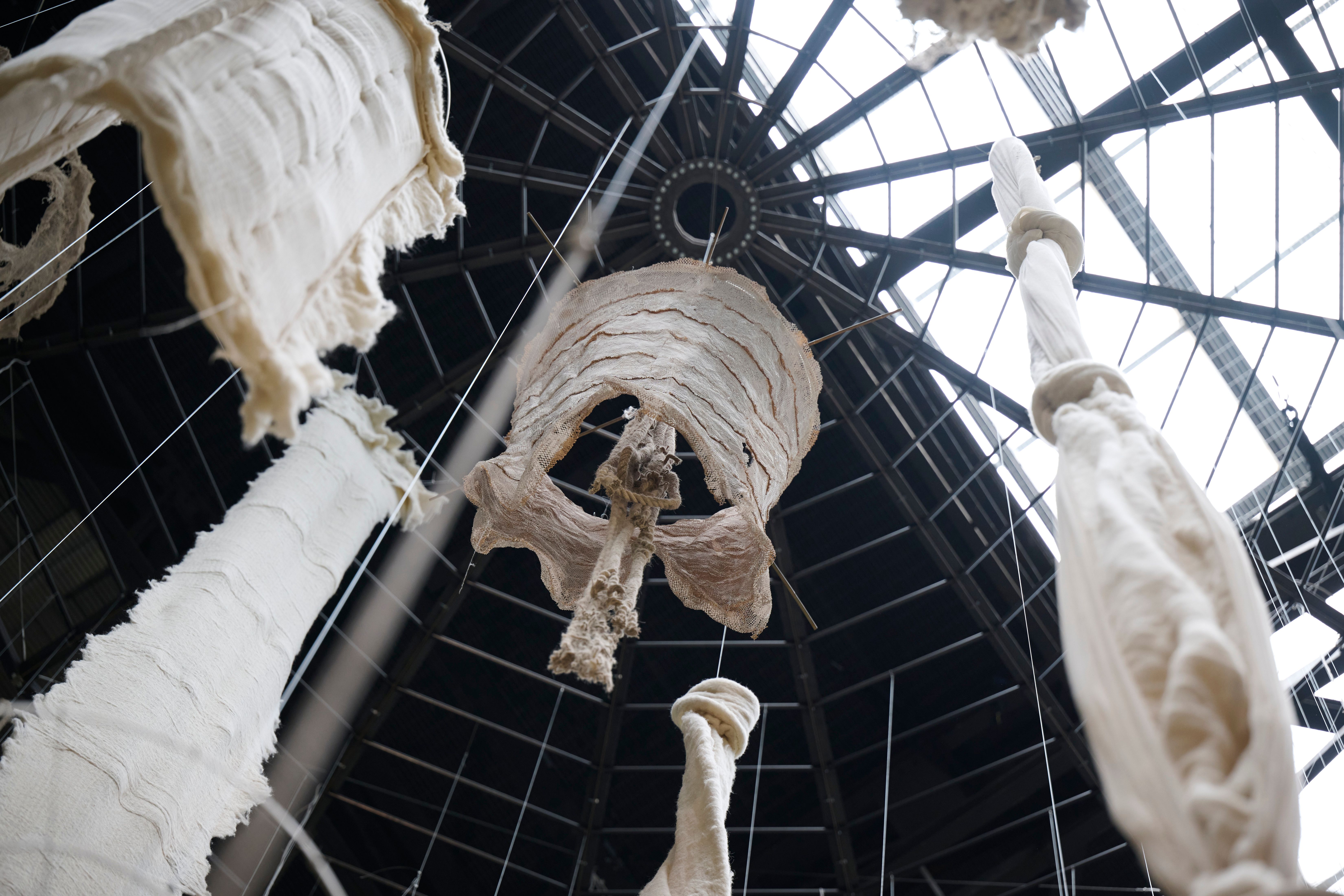 A symmetrical wind chime-inspired installation made of composite material hung from the ceiling, viewed from a worm's eye ...