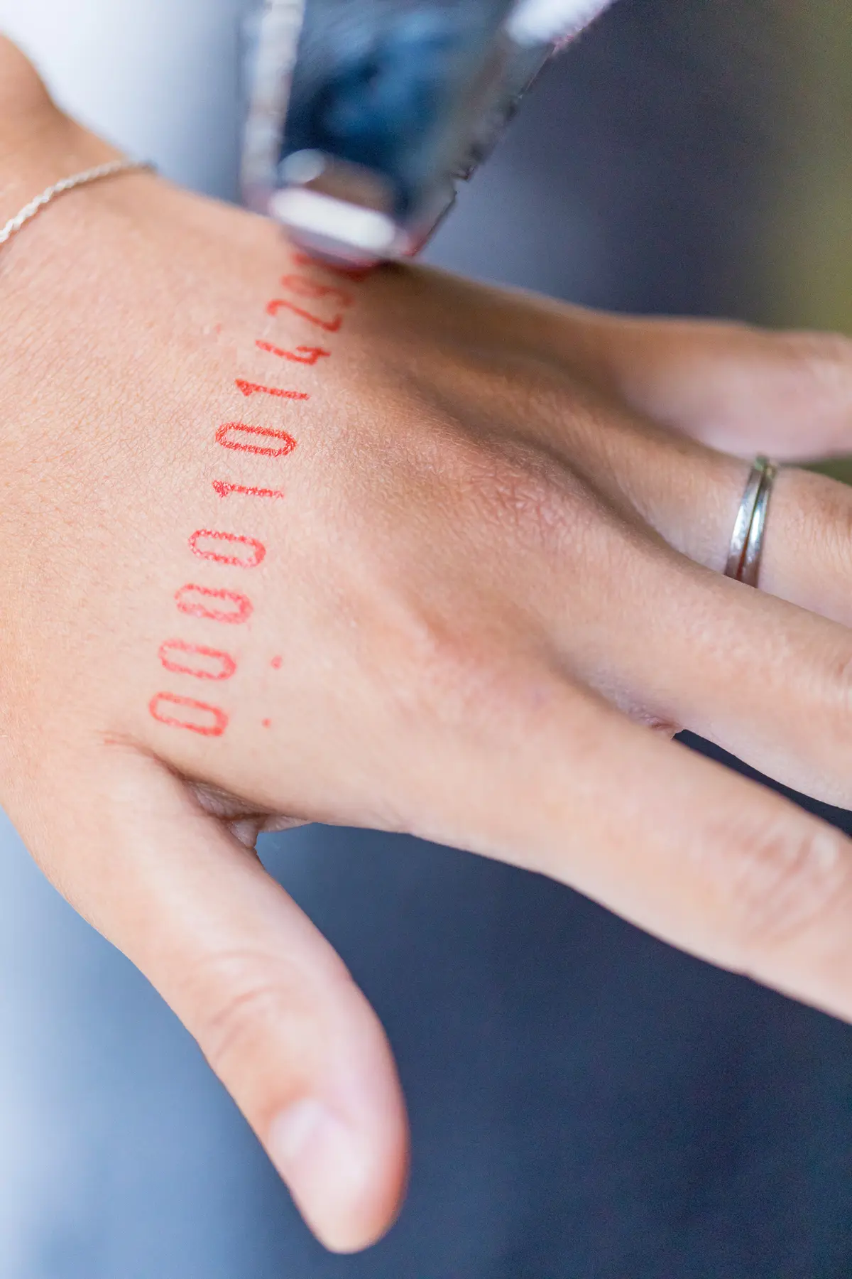 A hand adorned with a silver ring and a silver chain bracelet is being stamped with red numbers.